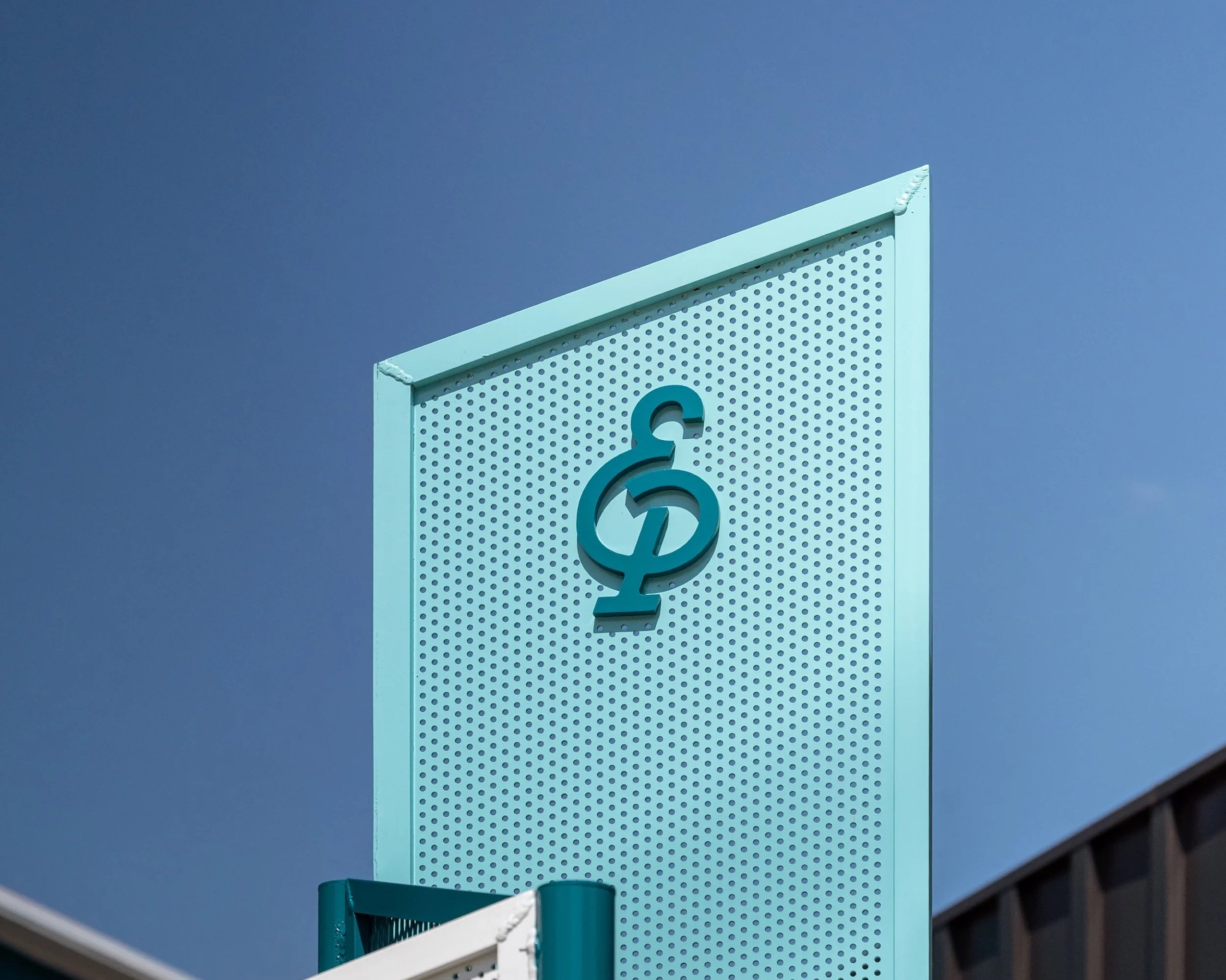 Close-up of a geometric modern building with a perforated pattern, featuring sharp edges, under a clear blue sky.