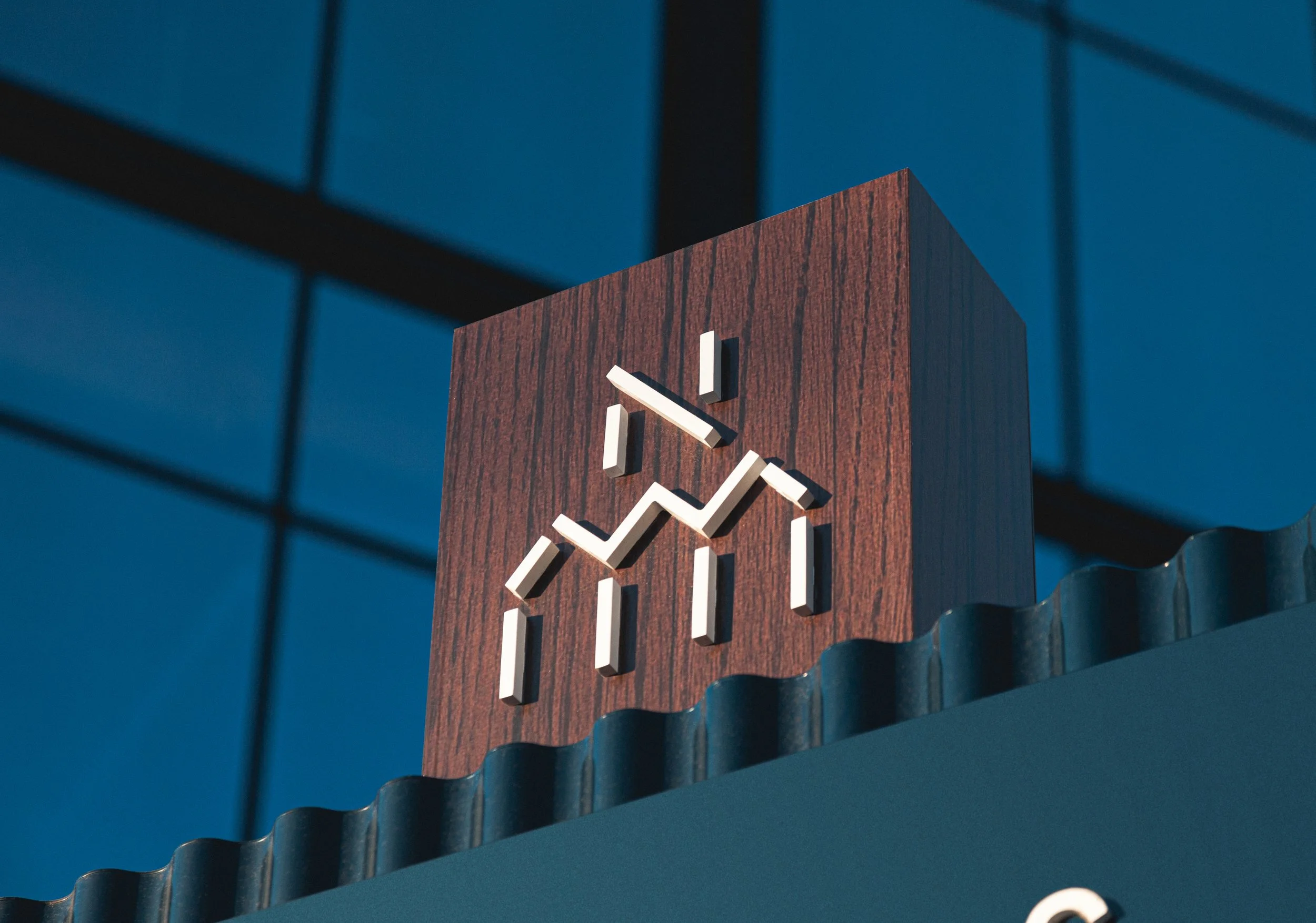 Close-up of a wooden wall clock with white hands and a dark blue wall background, seen through a pattern of black bars.