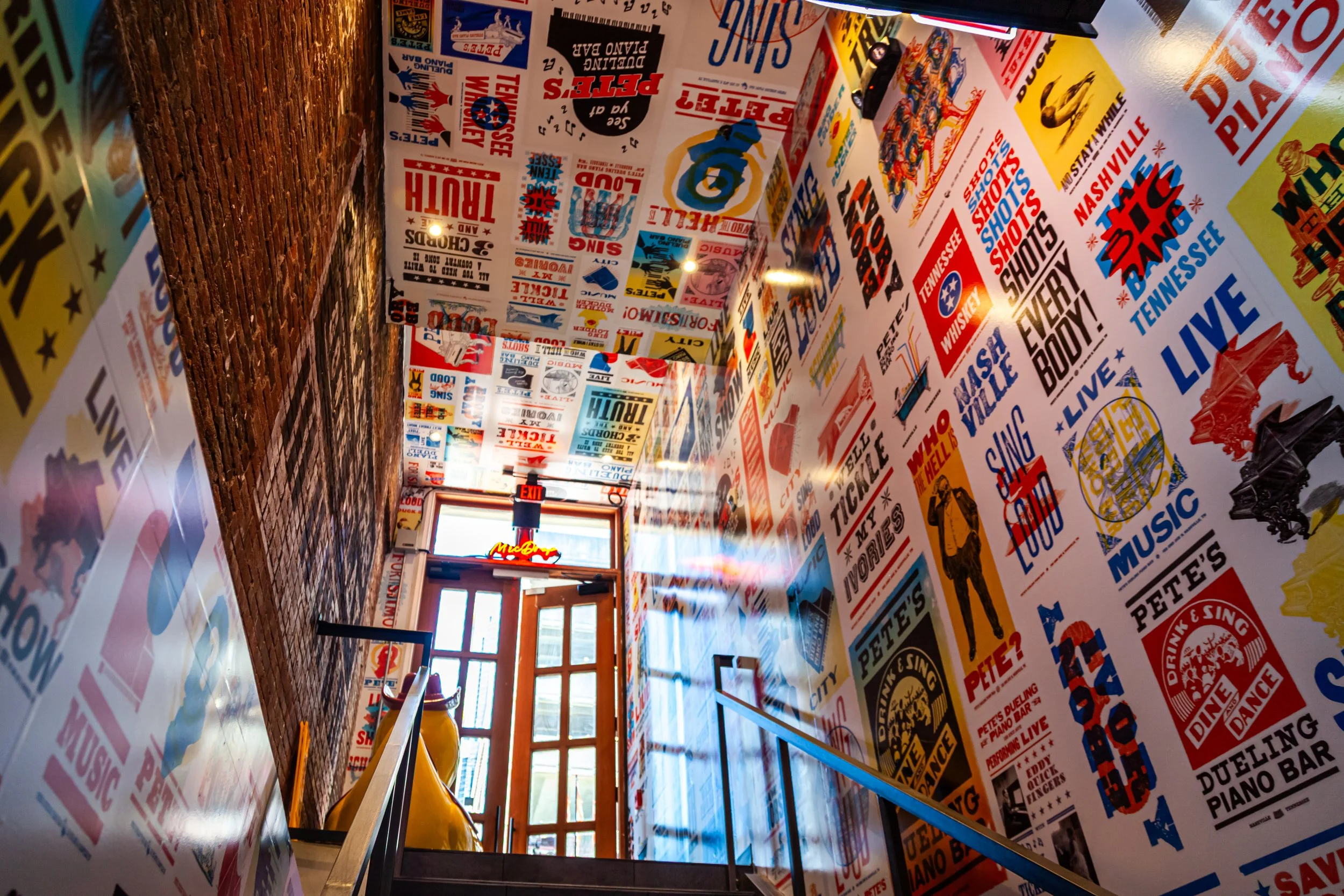Staircase leading down to a door with large windows, decorated with colorful vintage-style posters and signs on the walls.