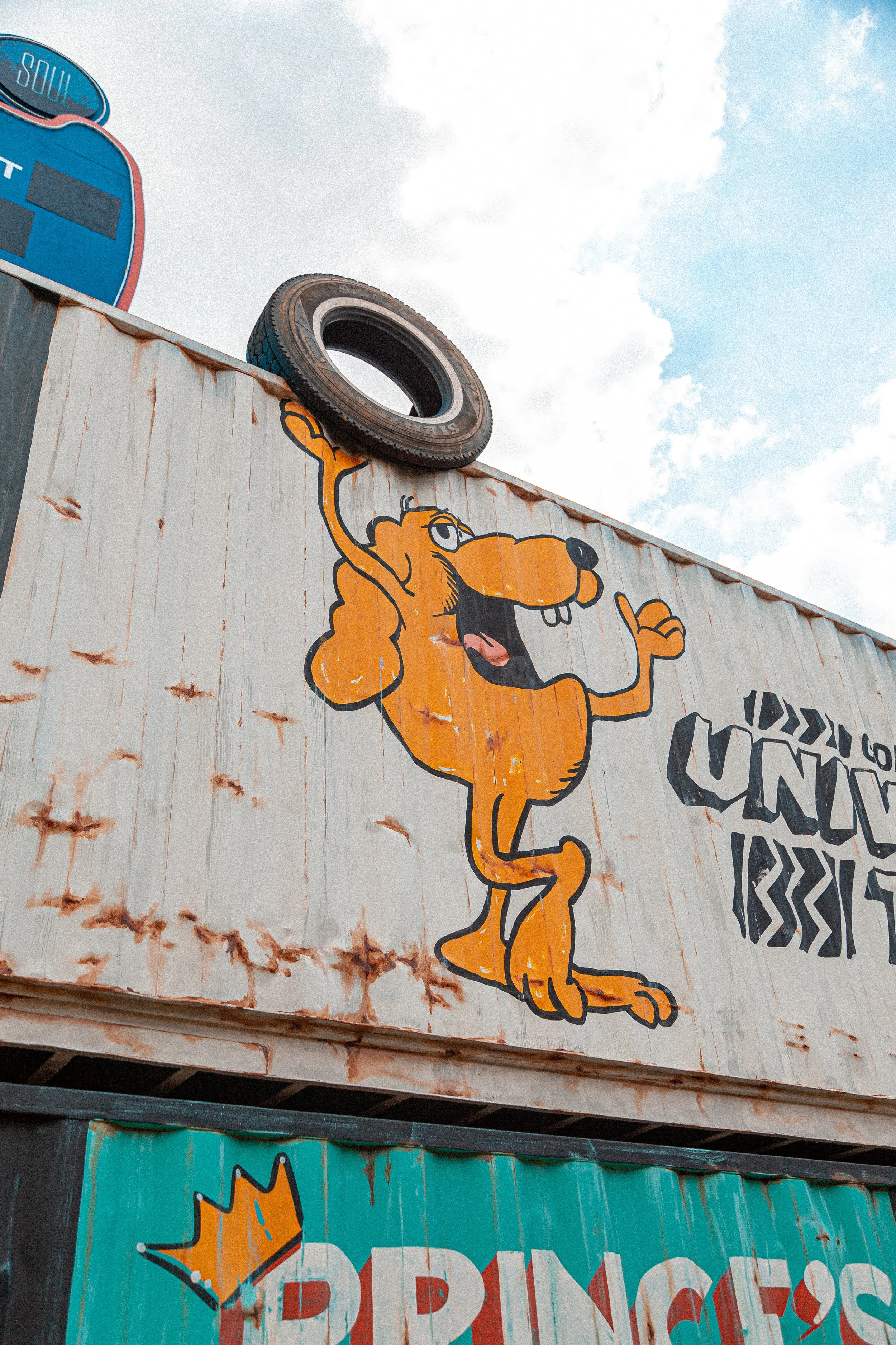 A painted cartoon lion character holding a royal scepter, with text and a crown graphic nearby, on a painted wall.
