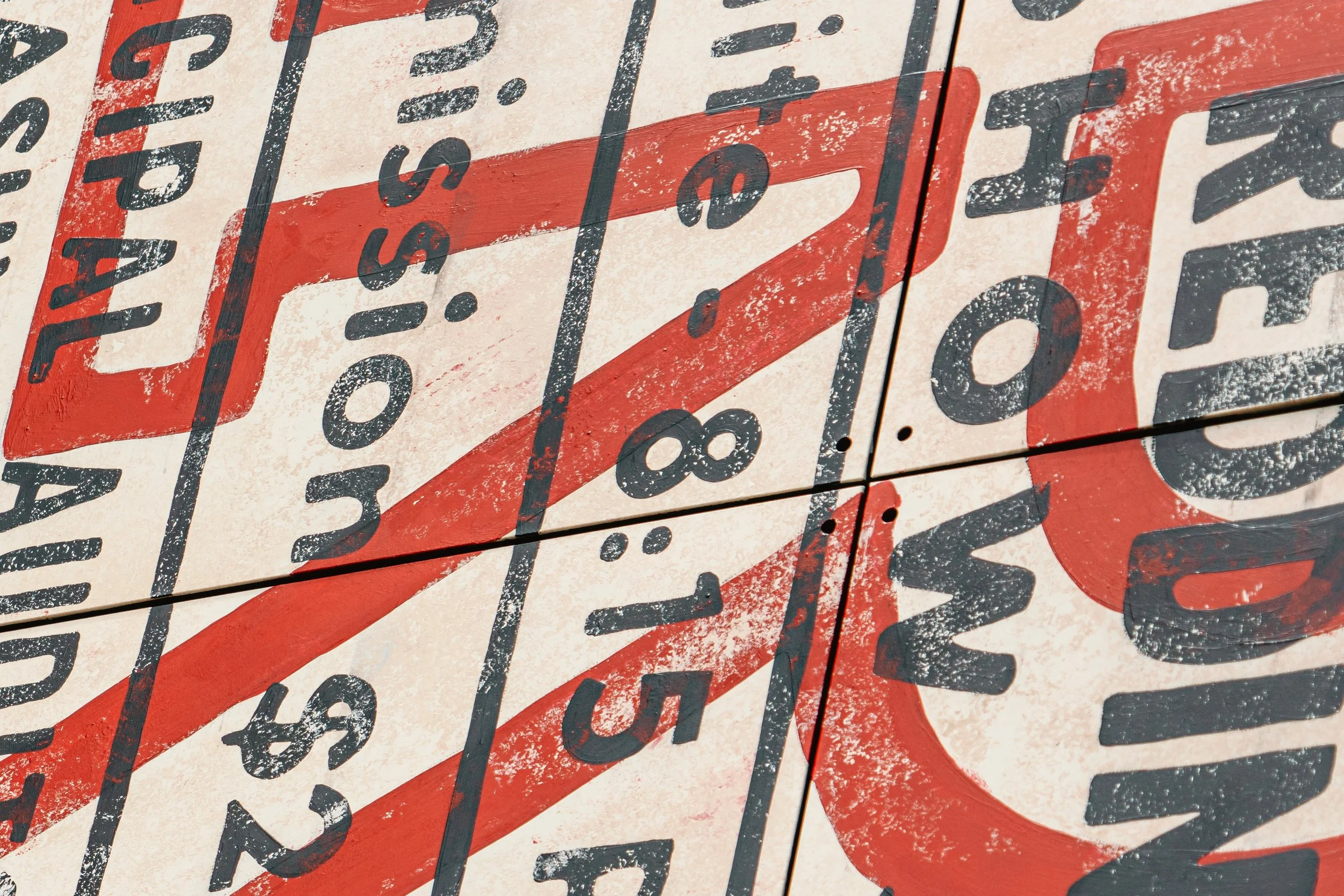 Close-up of a vintage-style sign displaying multiple numbers and words, with visible weathering and peeling paint, in black and red colors.