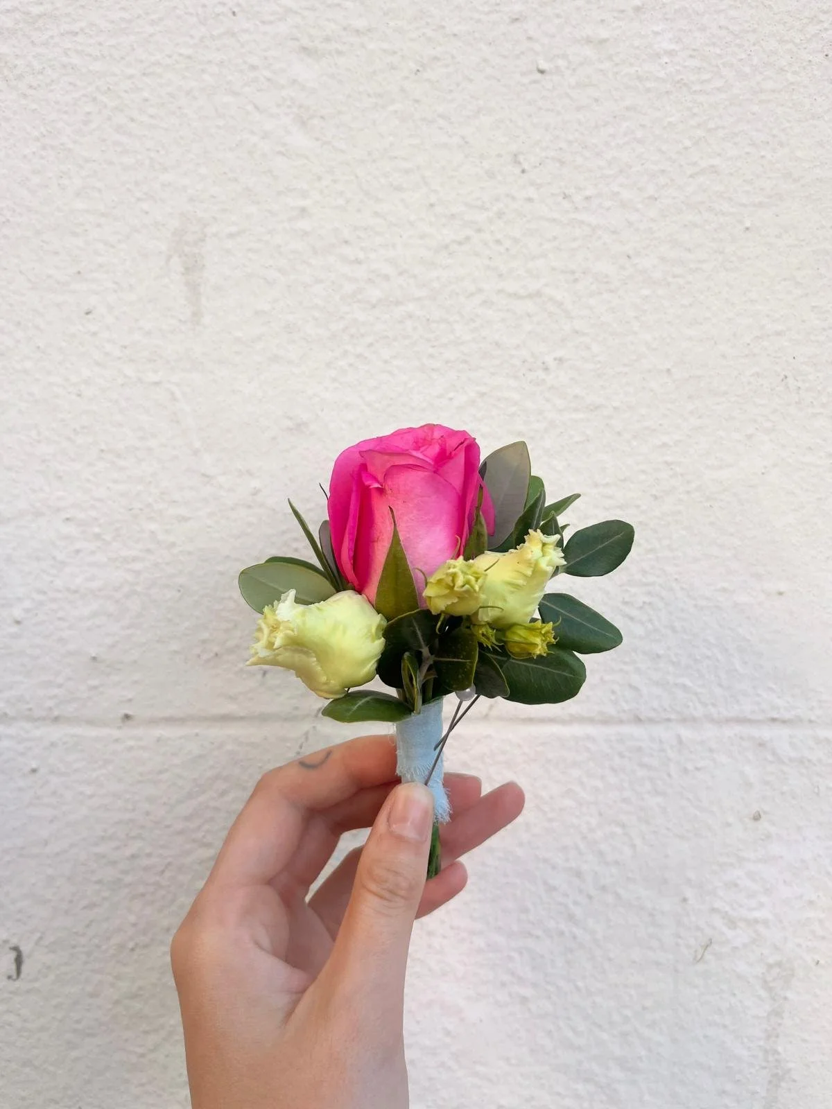 A person holding a small bouquet of roses against a plain white wall.