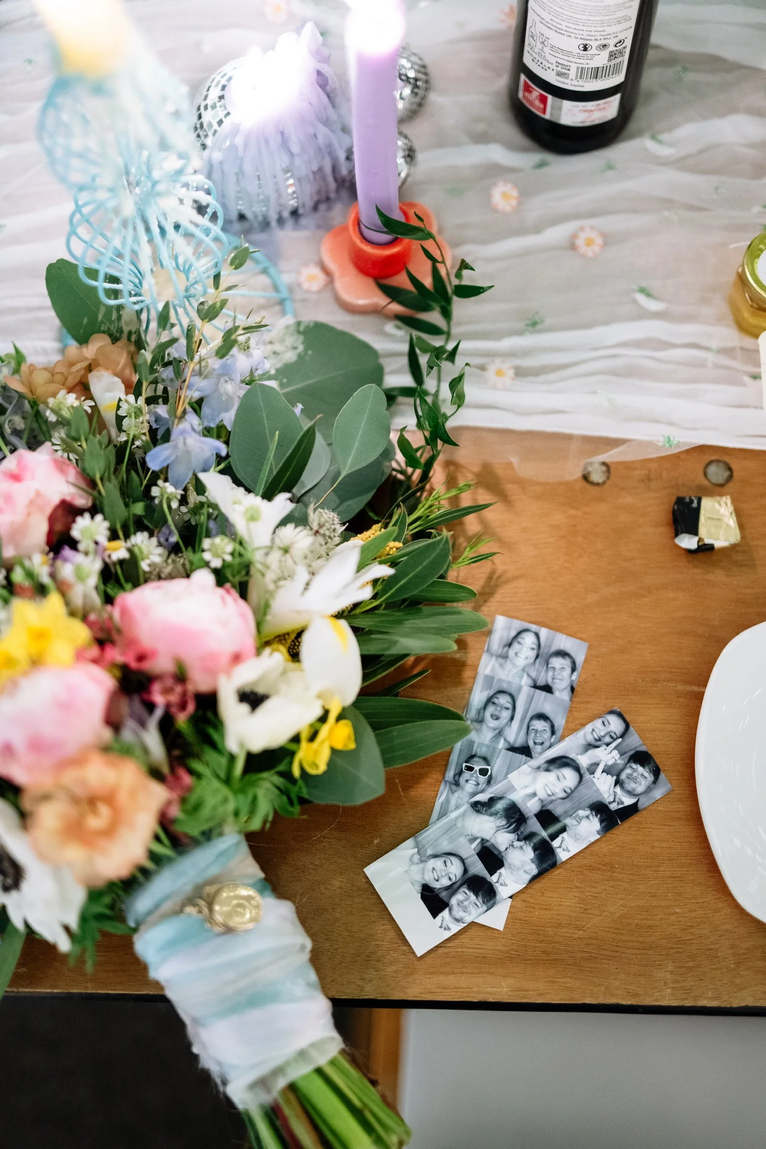 Colourful bridal bouquet with pink, white and blue flowers beside wedding photo strips.