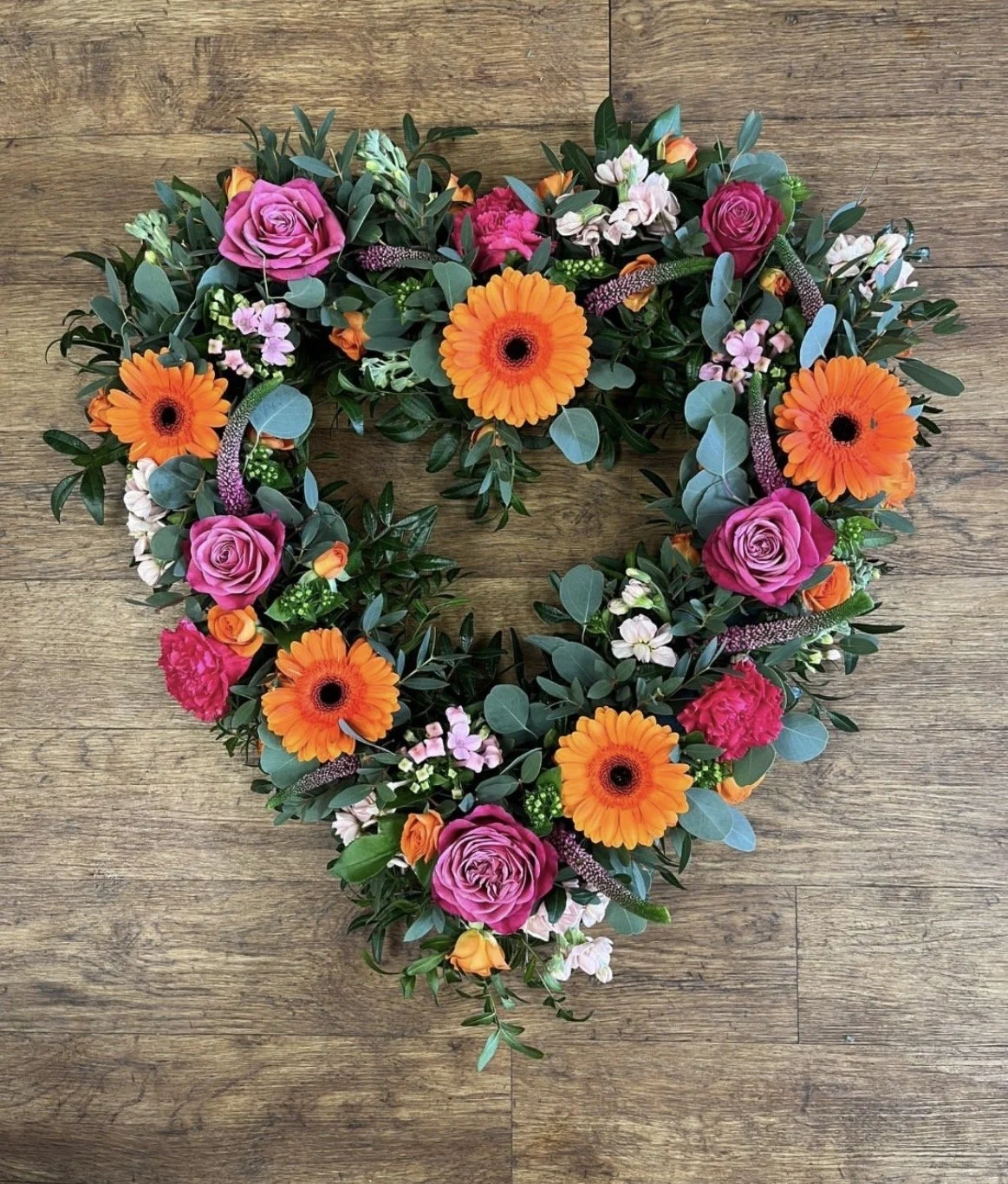 Colourful Heart shaped funeral flower arrangement with pink roses, orange gerberas and eucalyptus.