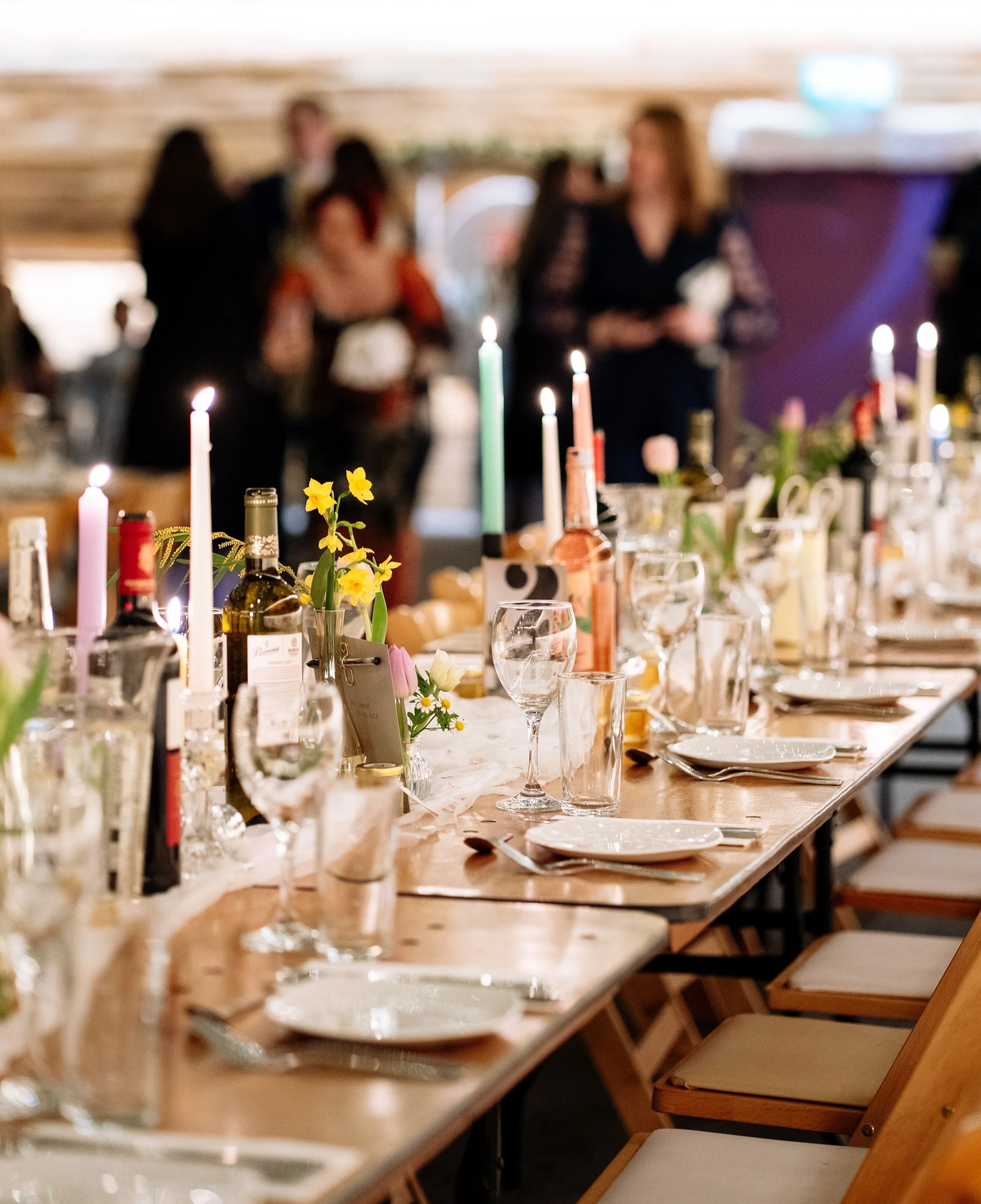 Wedding reception table styled with colourful candles and bud vases of spring flowers.