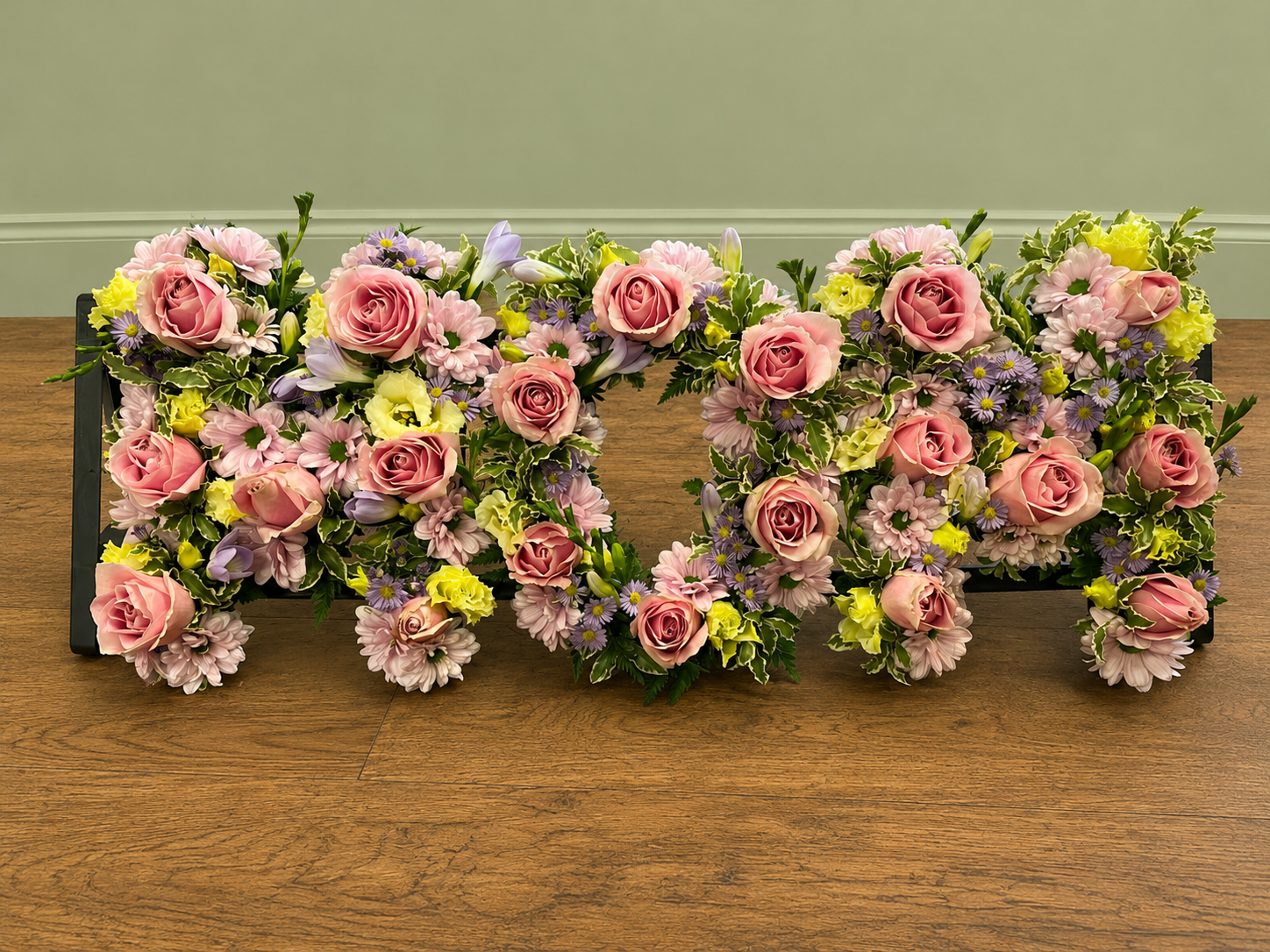 MOM funeral letter tribute with pink roses, lilac flowers and green foliage.