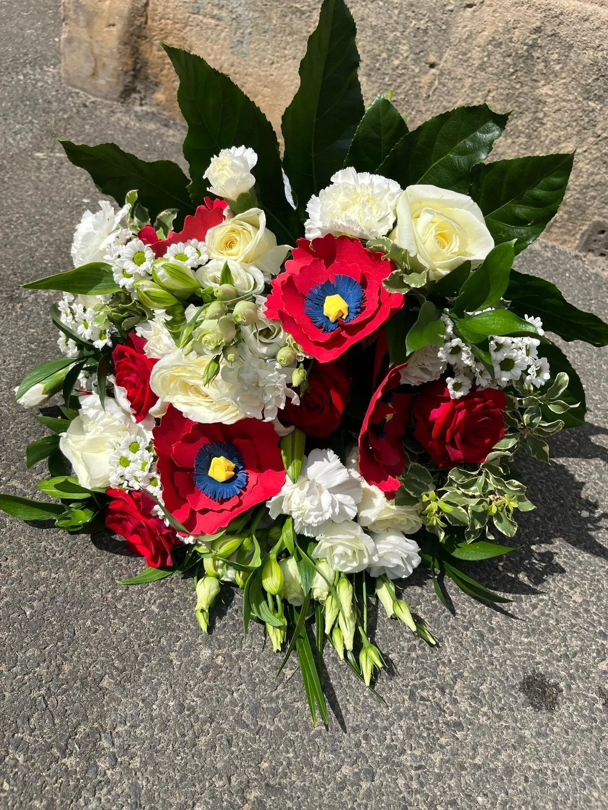 A colorful bouquet of flowers placed on a textured concrete surface, with large green leaves and a mix of white, red, and blue flowers.