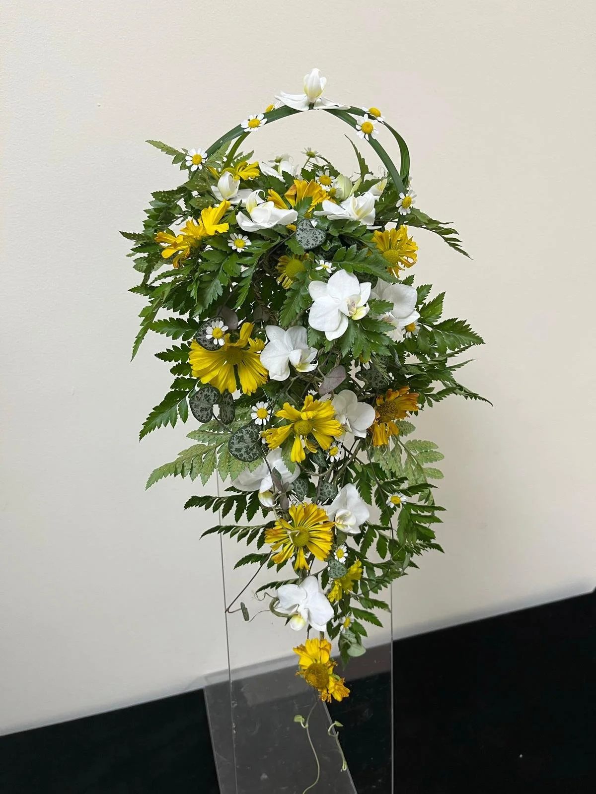 Artificial floral arrangement with white, yellow, and orange flowers, green leaves, and a decorative handle, displayed against a plain wall.