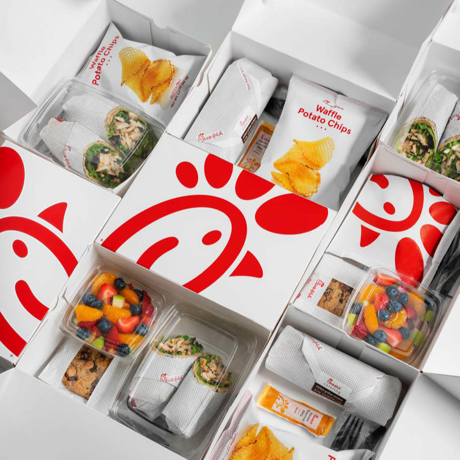 Chick-fil-A meal box with assorted food items including waffle potato chips, fruit salad, wrap sandwiches, granola bar, and assorted vegetables