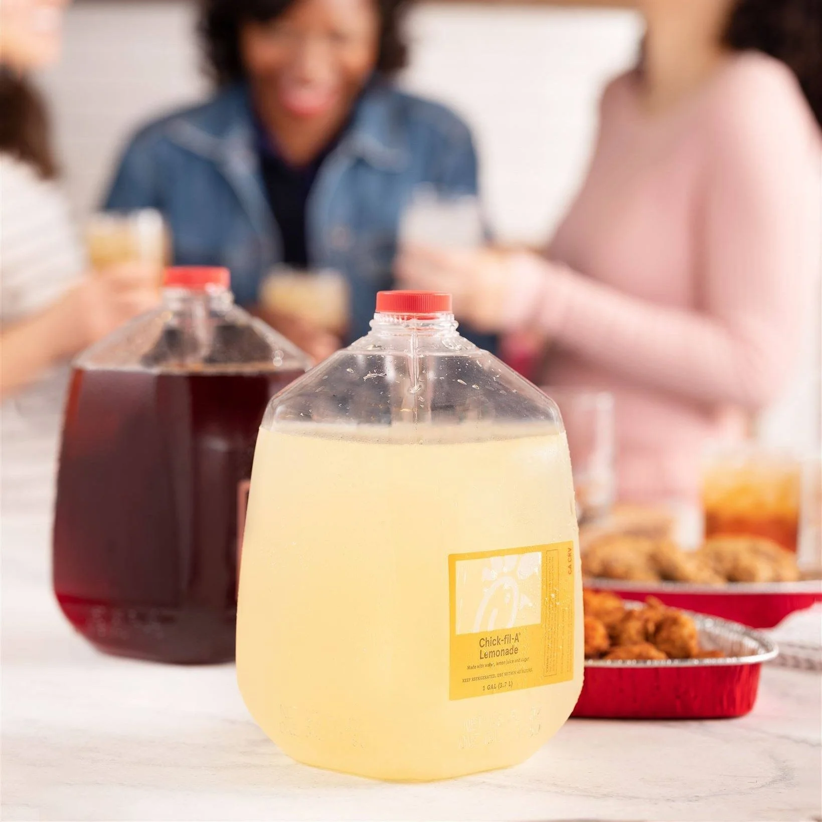 Close-up of a bottle of Chick-fil-A Lemonade on a table, with blurred people and food in the background.