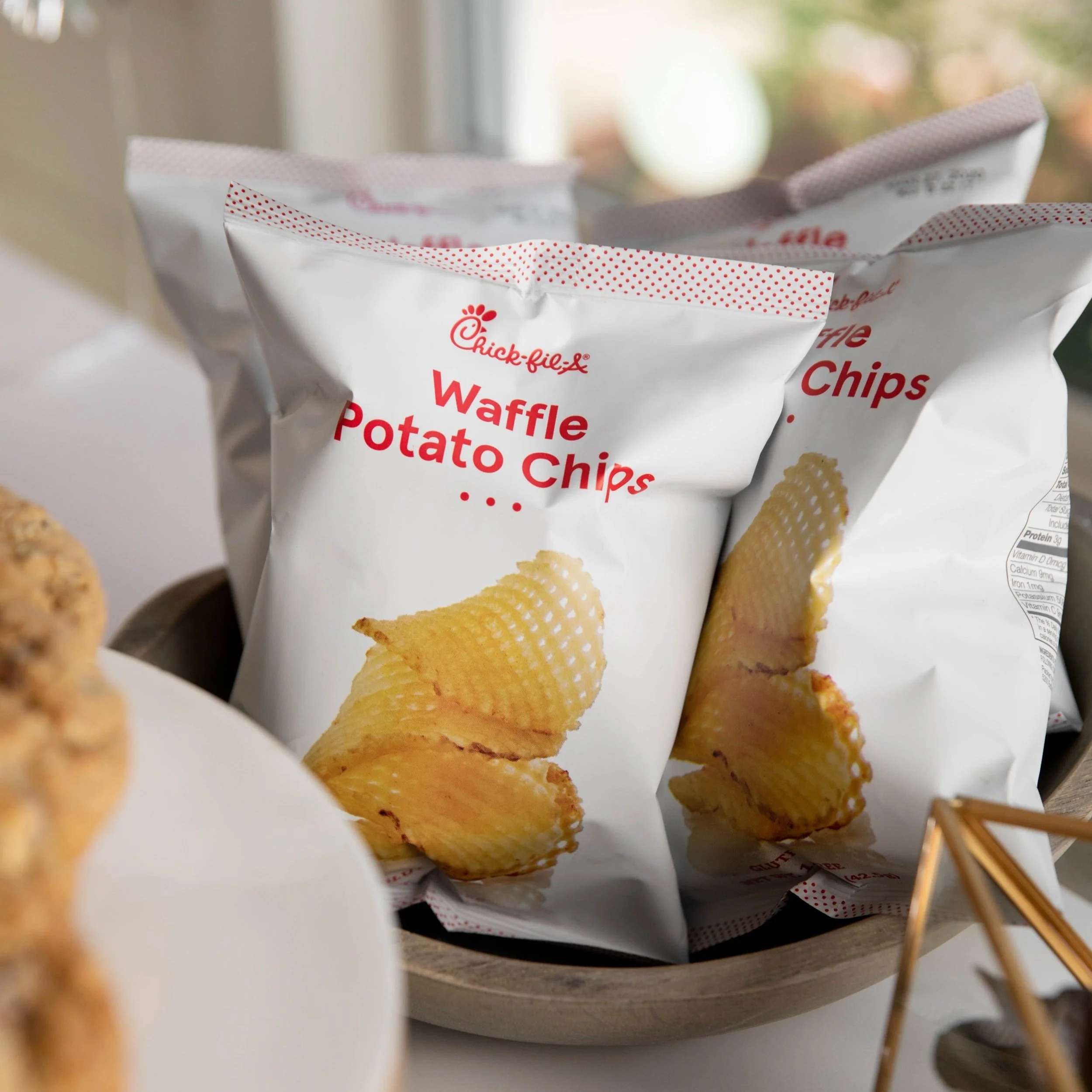 Bag of Chick-fil-A Waffle Potato Chips on a round tray with some snacks around.
