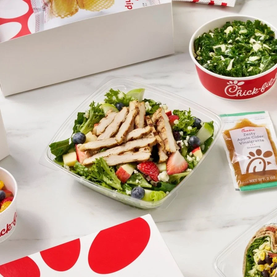 Chick-fil-A Chicken Salad with strawberries and blueberries, in a clear container, with a side of kale salad and apple cider vinegar dressing, on a white table.