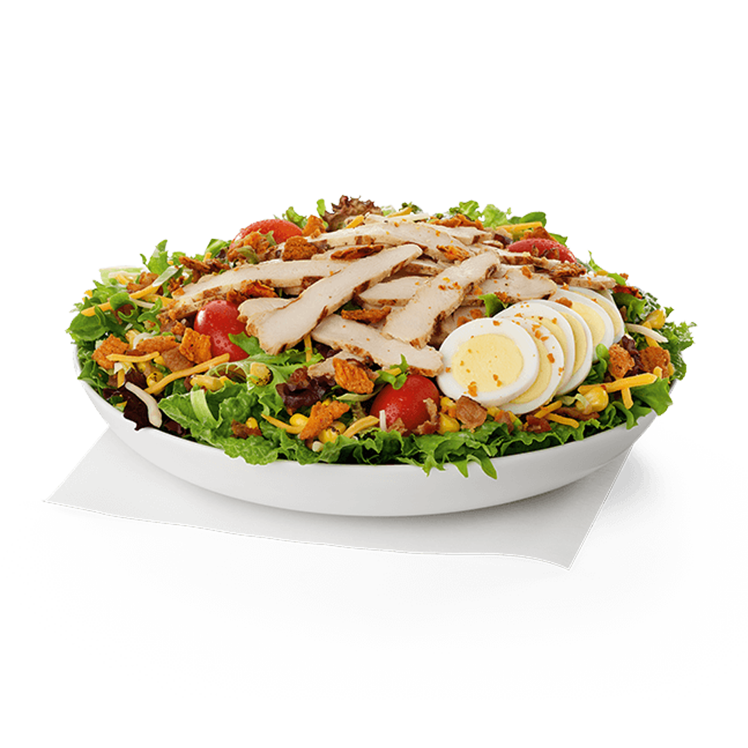 Salad with cherry tomatoes, shredded cheese, sliced chicken, hard-boiled egg slices, lettuce, bits of bacon, and crunchy toppings in a white bowl.