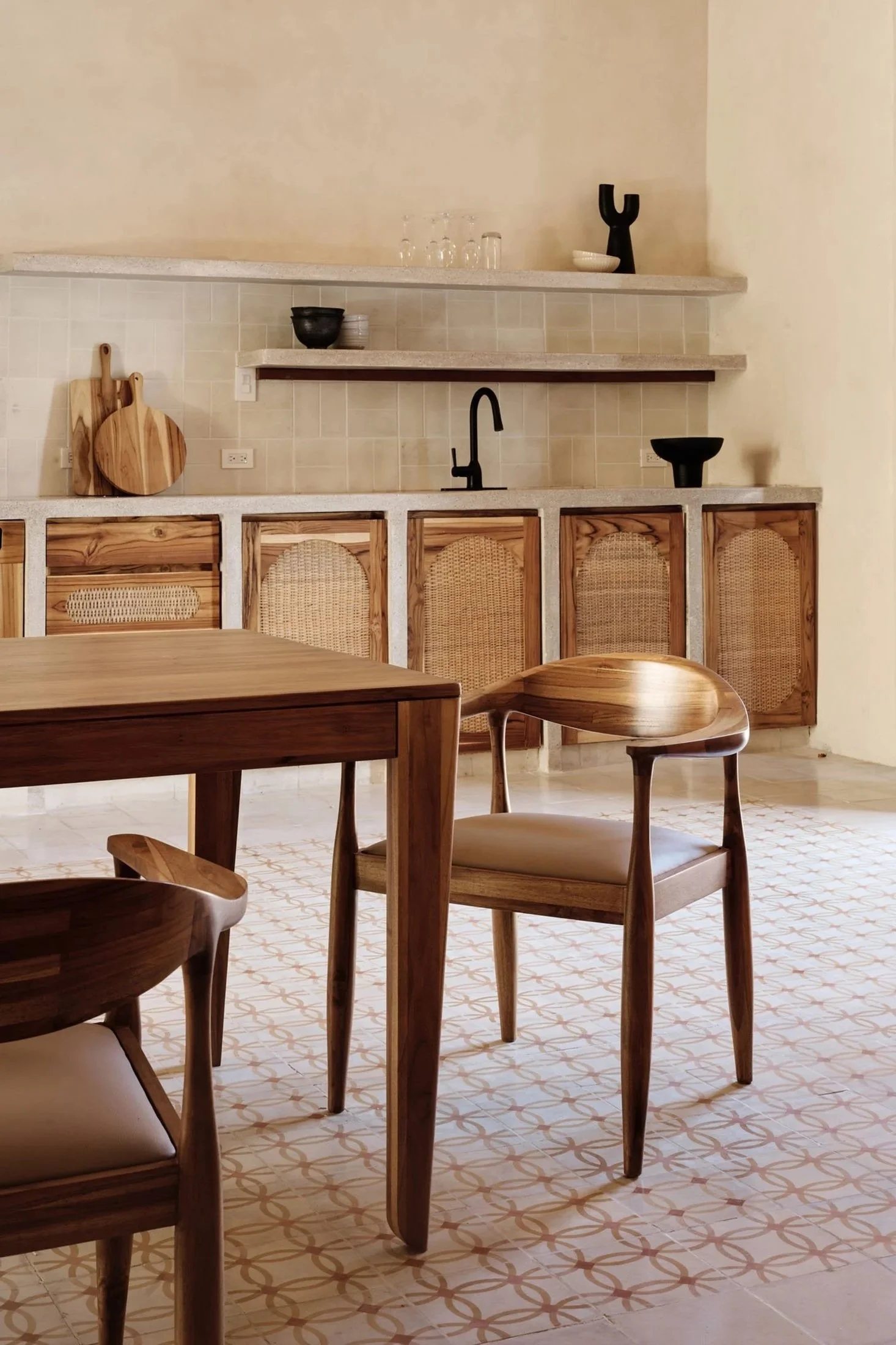 A modern kitchen with wooden chairs, a patterned floor, light-colored countertops, black and white bowls, and decorative black figurines on gold floating shelves.