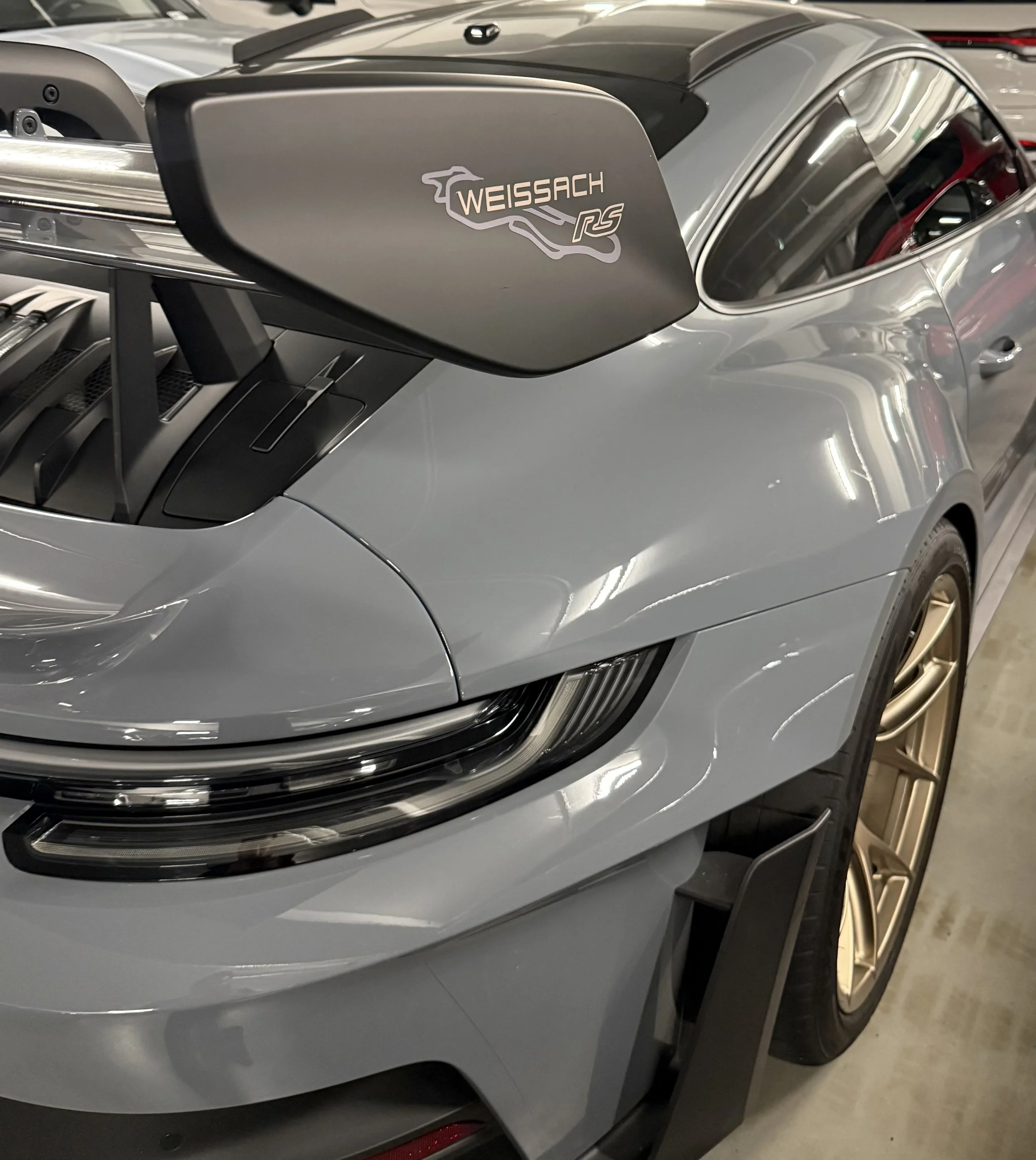 Close-up of a silver sports car with a Weissach RS badge on a side mirror, parked in a garage or showroom.