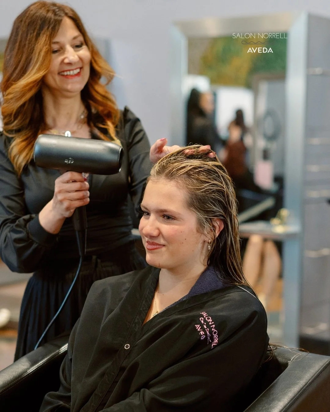 Nina — dimensional brunette, balayage, and lived-in color specialist at Salon Norrell AVEDA in Carrollwood Tampa doing a bouncy blowout