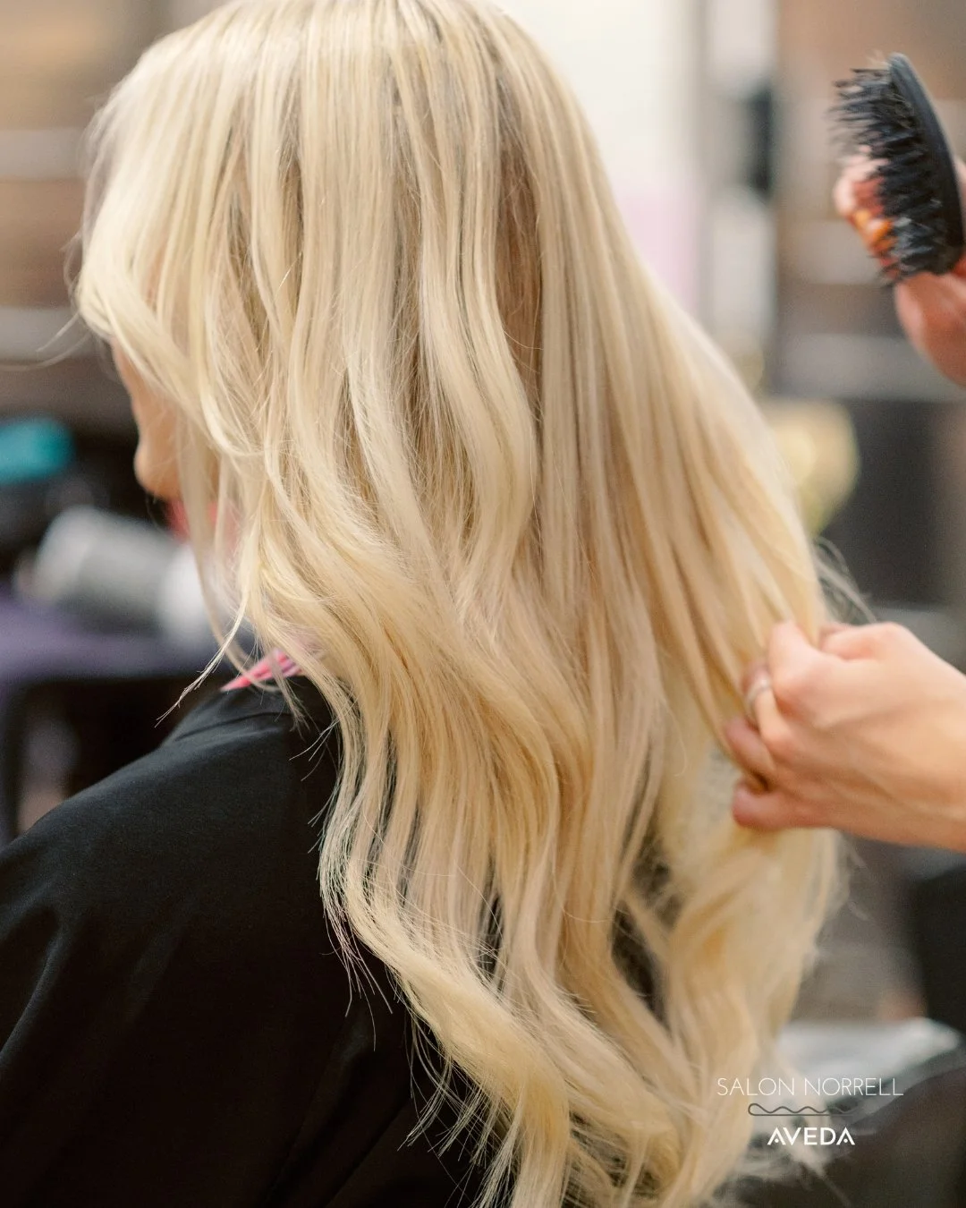 100% human hair extensions with lived-in blonde color and soft waves styled at Salon Norrell AVEDA in Hyde Park Tampa