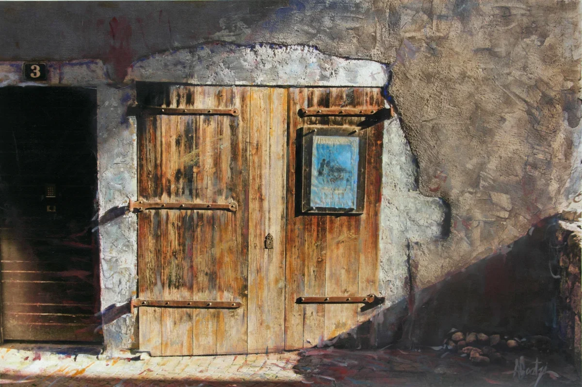 A rustic wooden door with a small framed picture hanging on it, set into a stone and concrete wall with a small black door to the left.