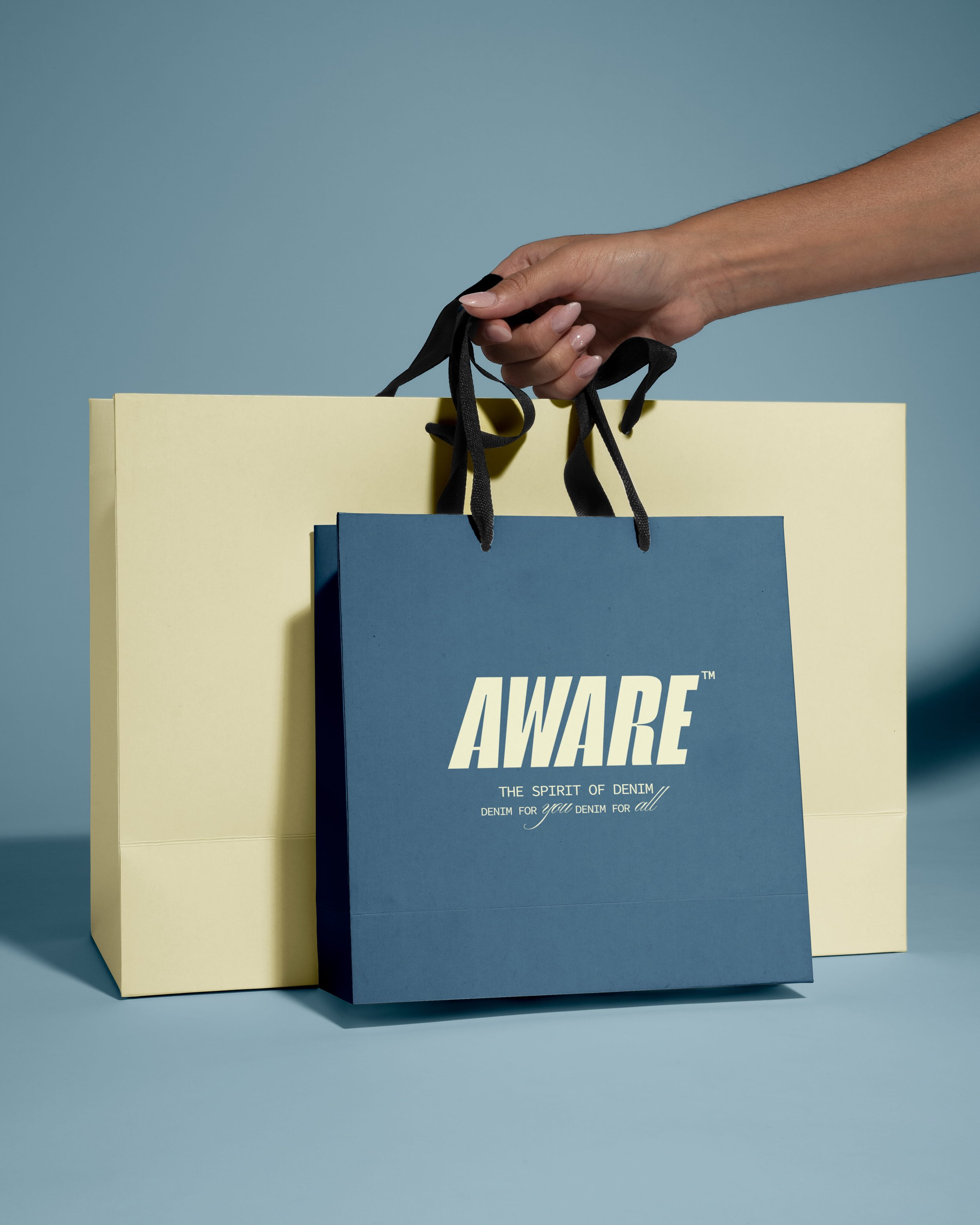 Close-up of a hand holding black ribbon handles of blue and yellow shopping and gift bags against a blue background.