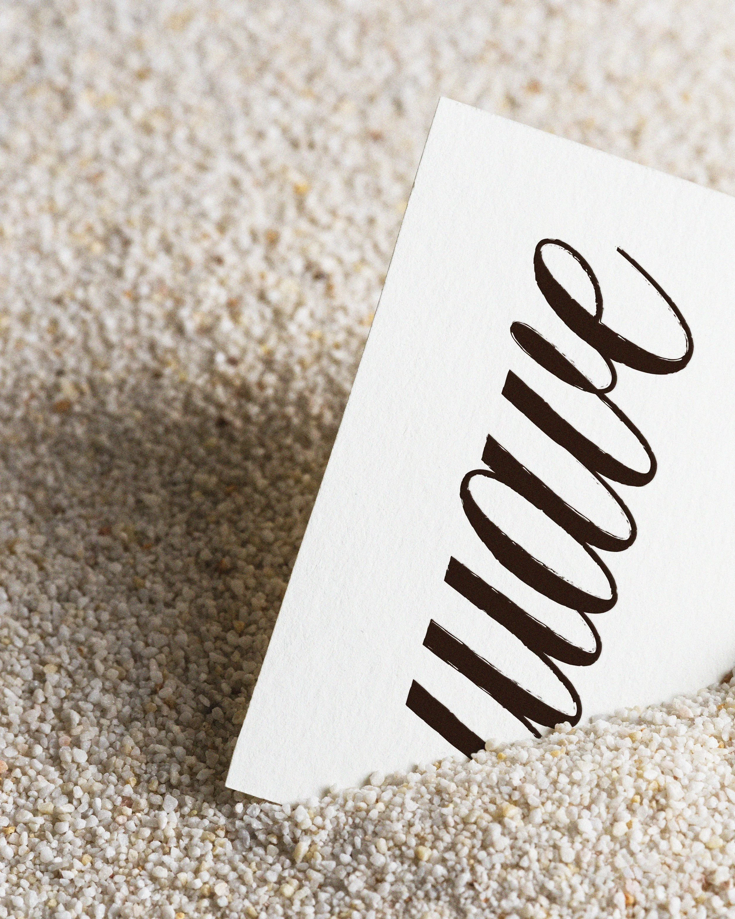 Close-up of a white paper with handwritten black text, placed on a surface covered with small white pebbles.