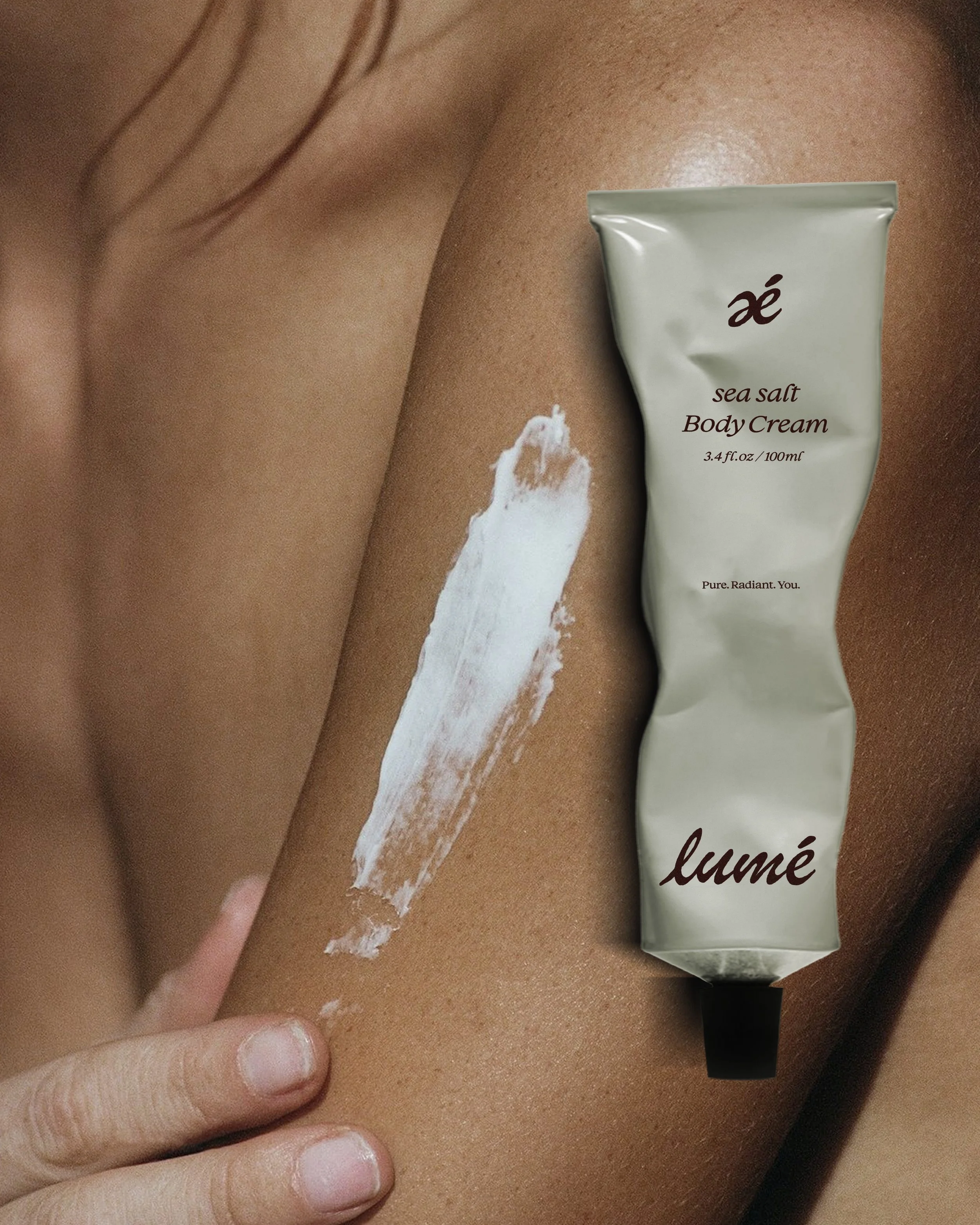 Close-up of a person's skin with a hand applying white cream from a tube labeled 'lumé' onto their shoulder.