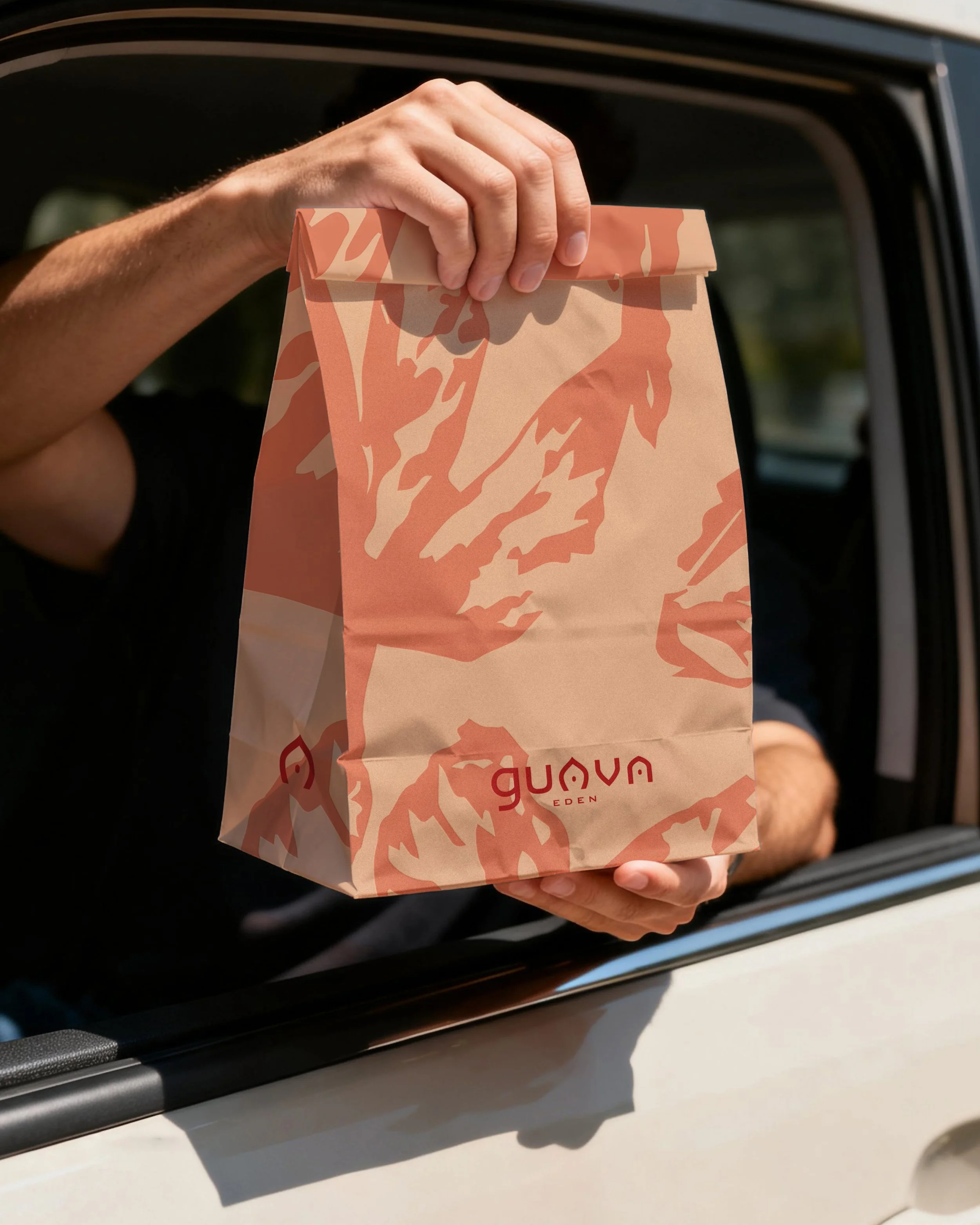 A person holding a paper bag with orange and beige abstract patterns while leaning out of a car window.