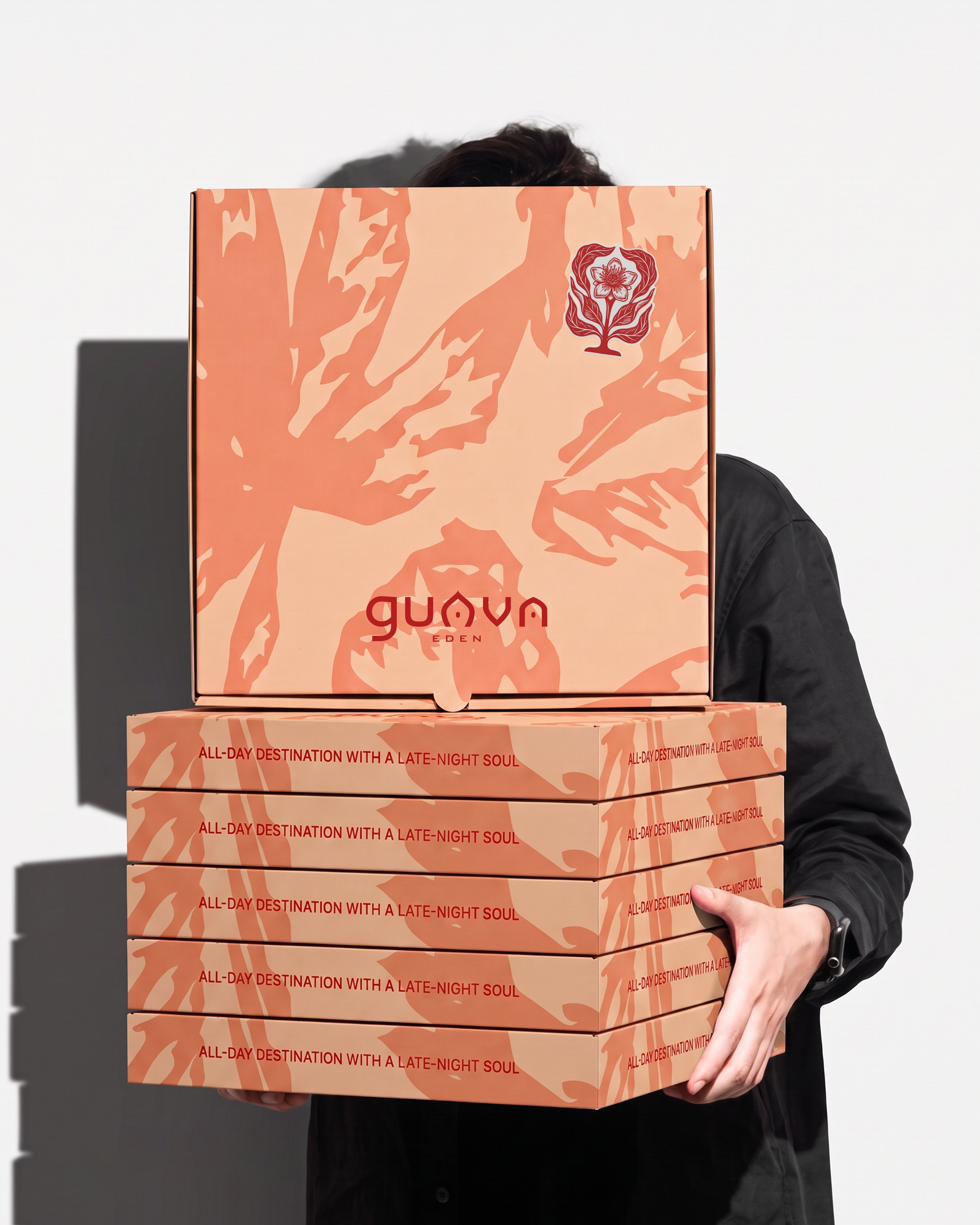 Person in black jacket holding two stacked boxes with a peach and orange floral pattern and the text "ALL-DAY DESTINATION WITH A LATE-NIGHT SOUL".