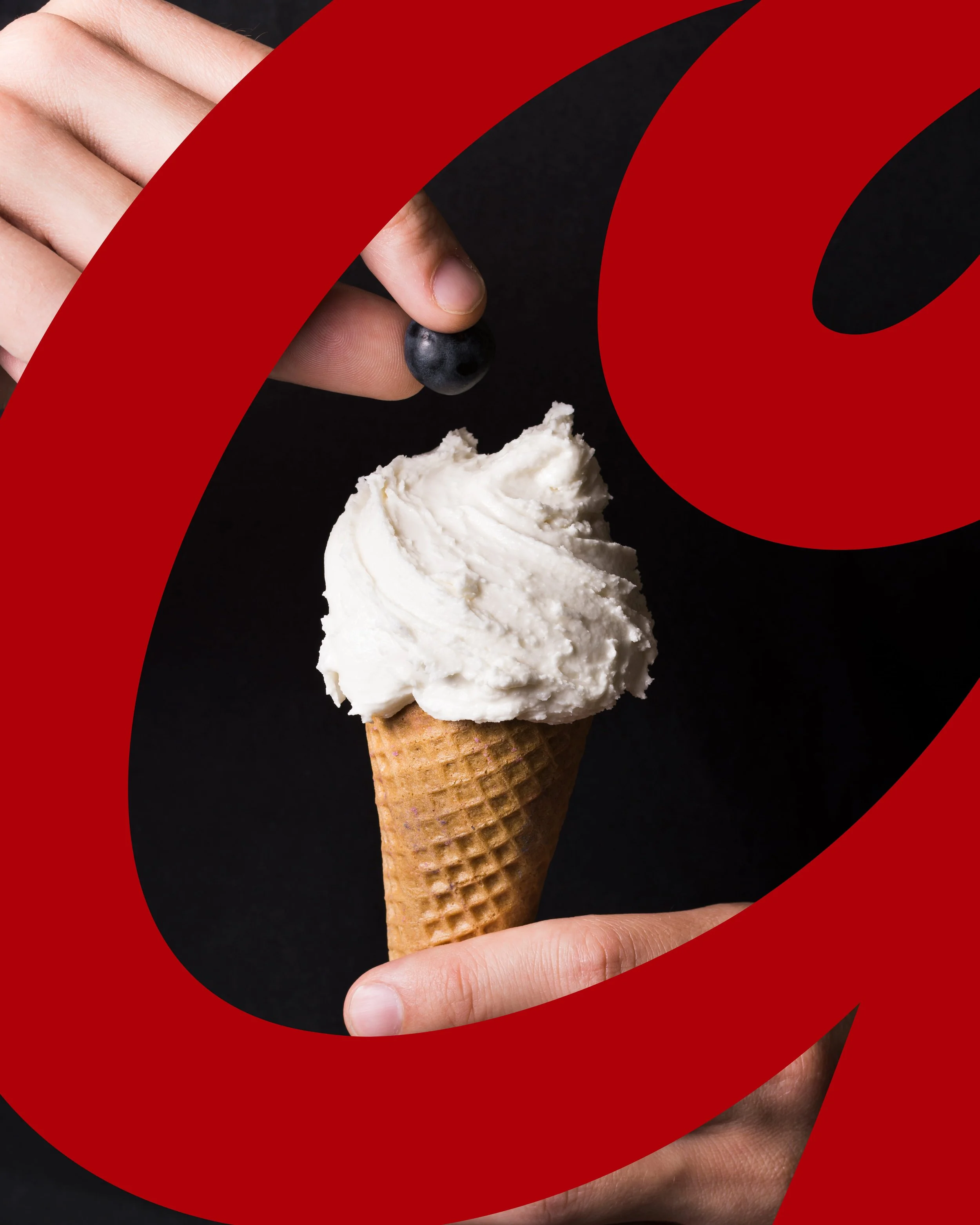 A person holding an ice cream cone topped with vanilla ice cream and a single blueberry. The background is black, partially covered by a red, curved graphic element.