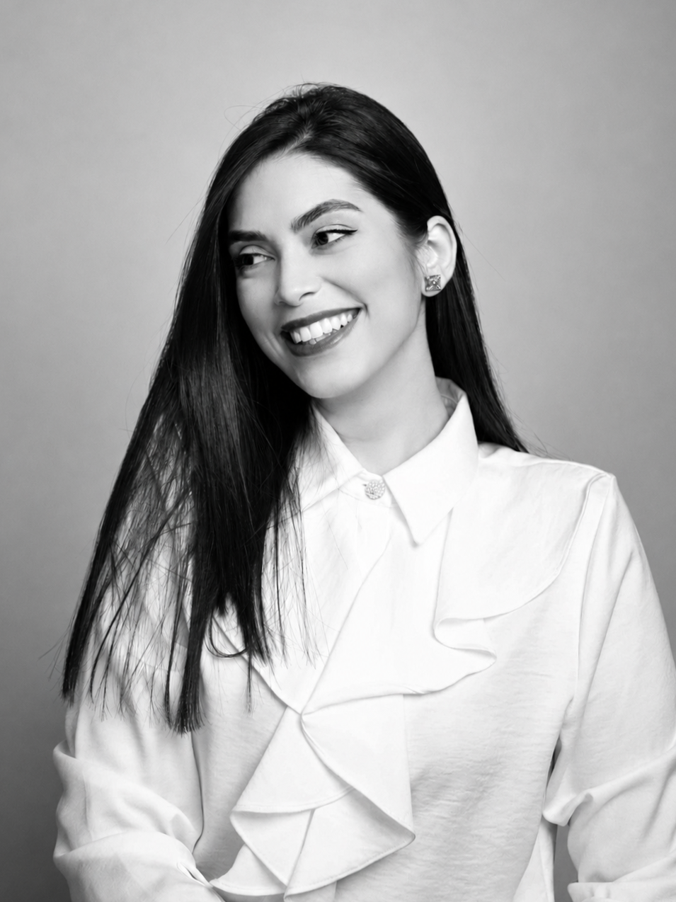 Black and white portrait of a young woman with long dark hair, smiling and looking to the side, wearing a white blouse with ruffles.