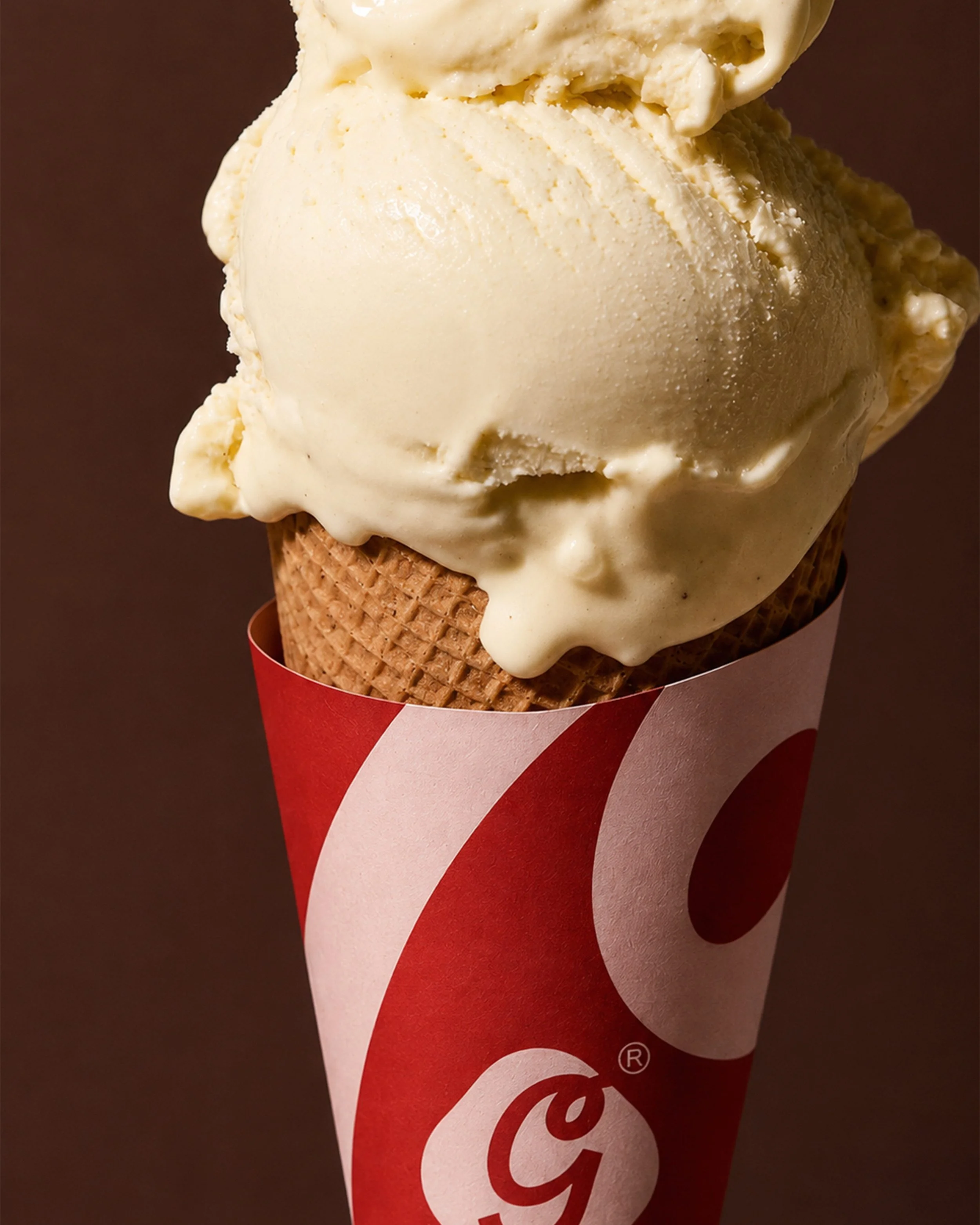 Close-up of a vanilla ice cream cone in a red and white paper wrapper, with a textured waffle cone at the bottom.