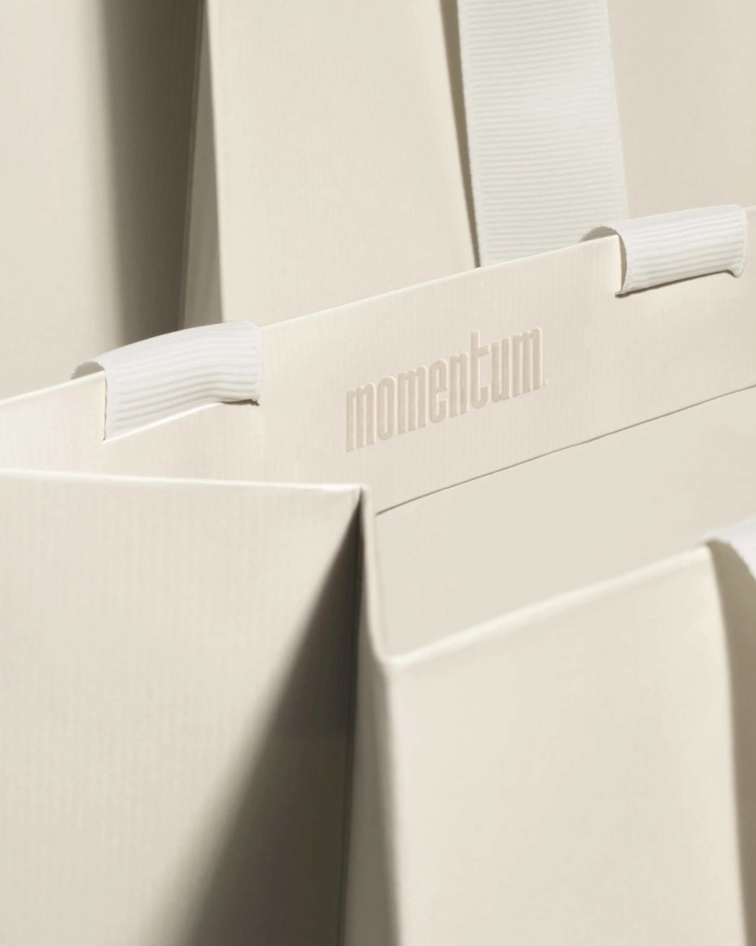 Close-up of a white cardboard box with the word 'moment' embossed on its side, and a textured white handle or strap attached to the box.