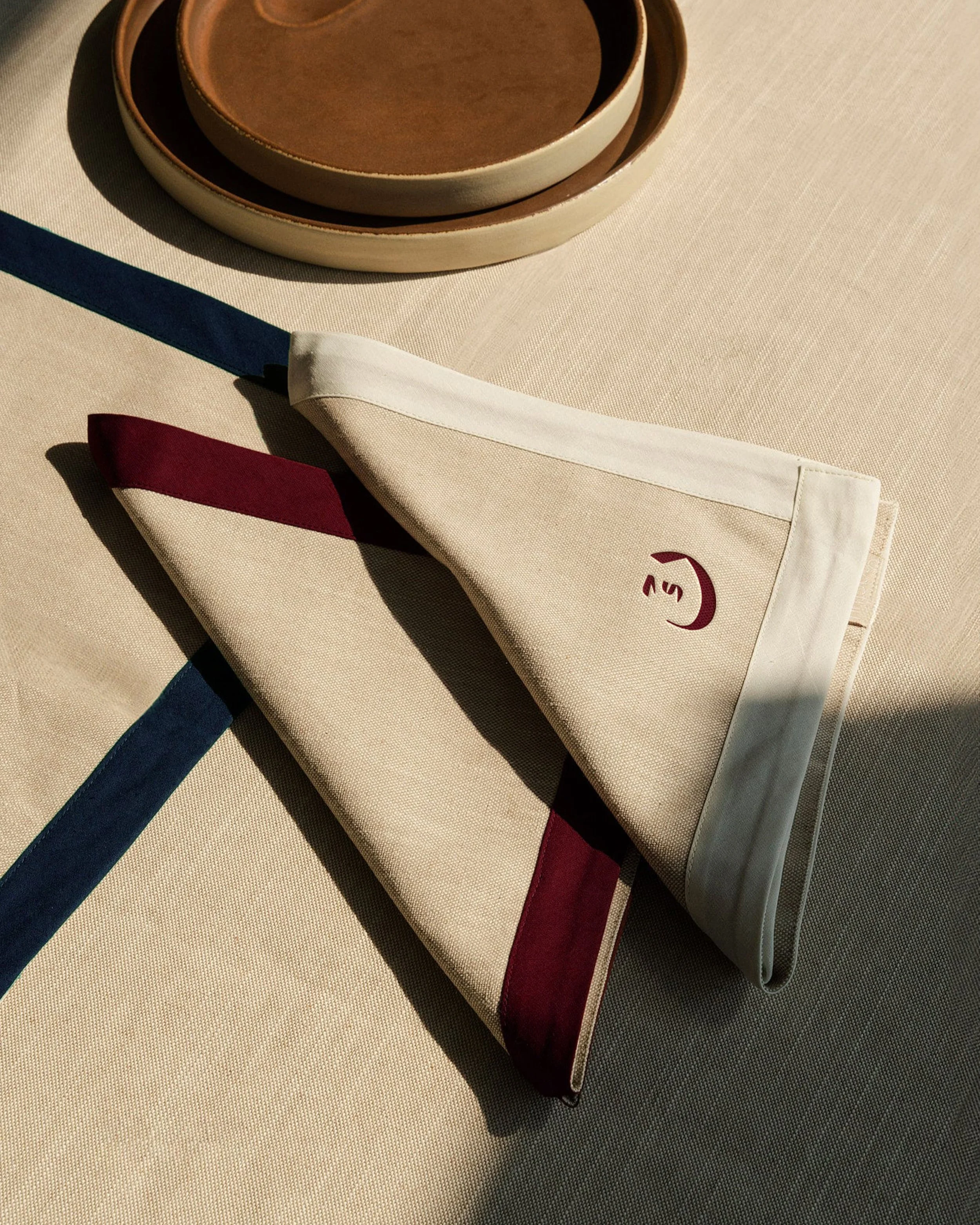 Stacked ceramic bowls in various shades of brown on a cloth surface, with a cloth bag featuring a maroon and navy colored design