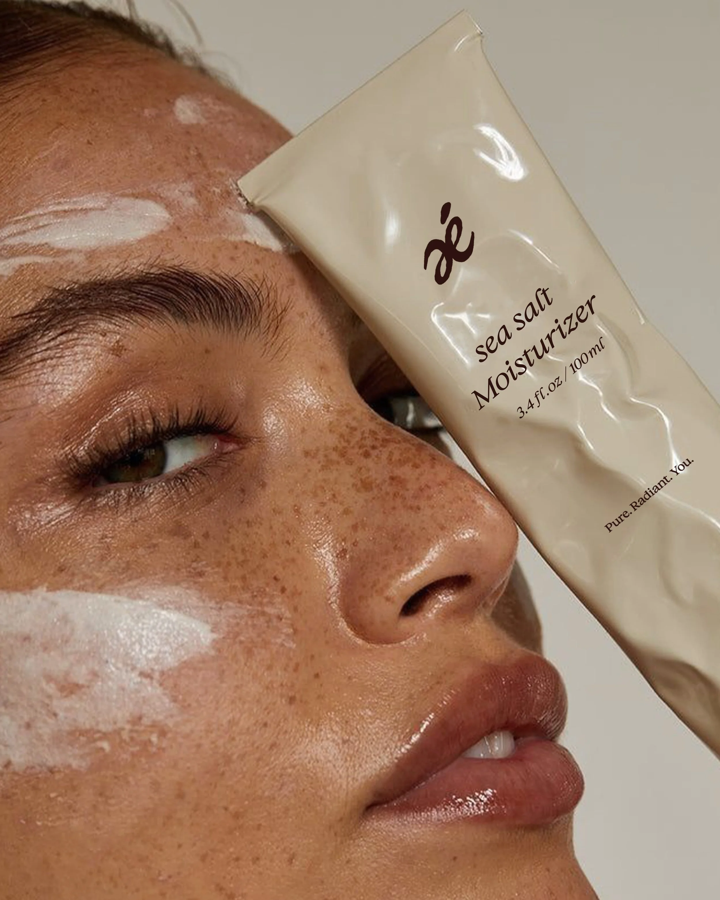 A person with freckles applying sea salt moisturizer on their face, with the tube partially covering their face.