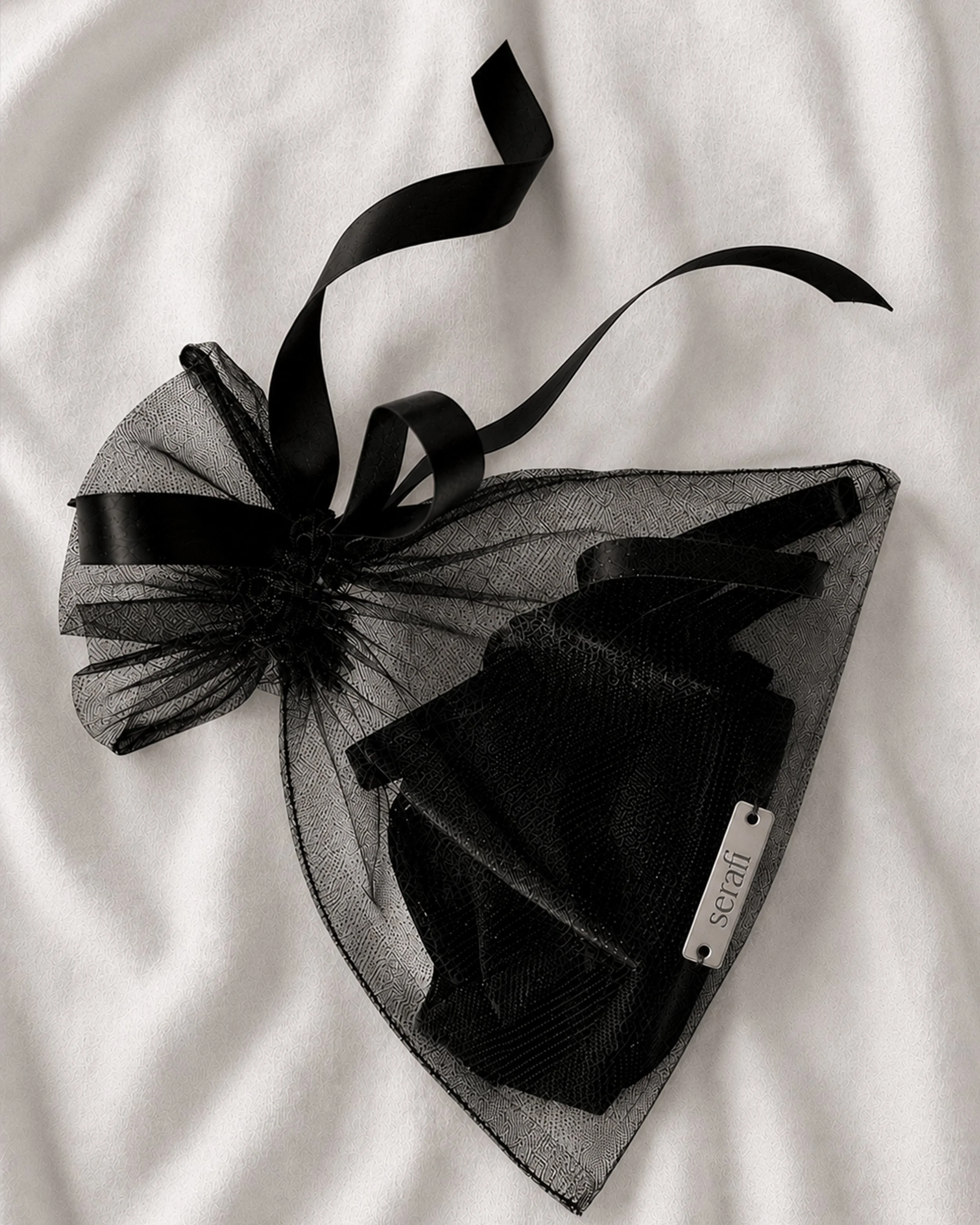 A black and white bridal corsage with black ribbons and a white tag labeled 'Seraf' on a white textured fabric background.