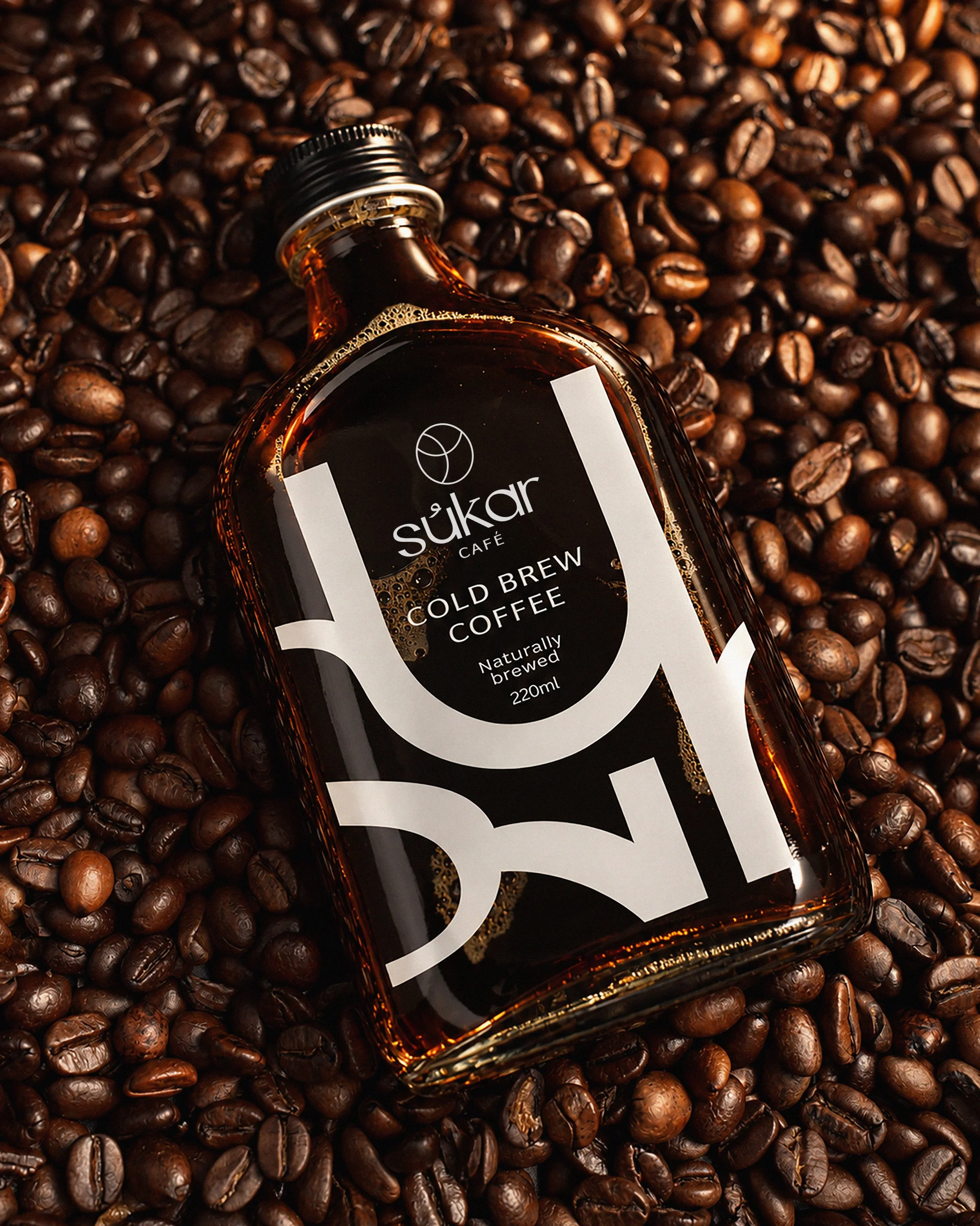 A bottle of Sukar cold brew coffee resting on a bed of roasted coffee beans.