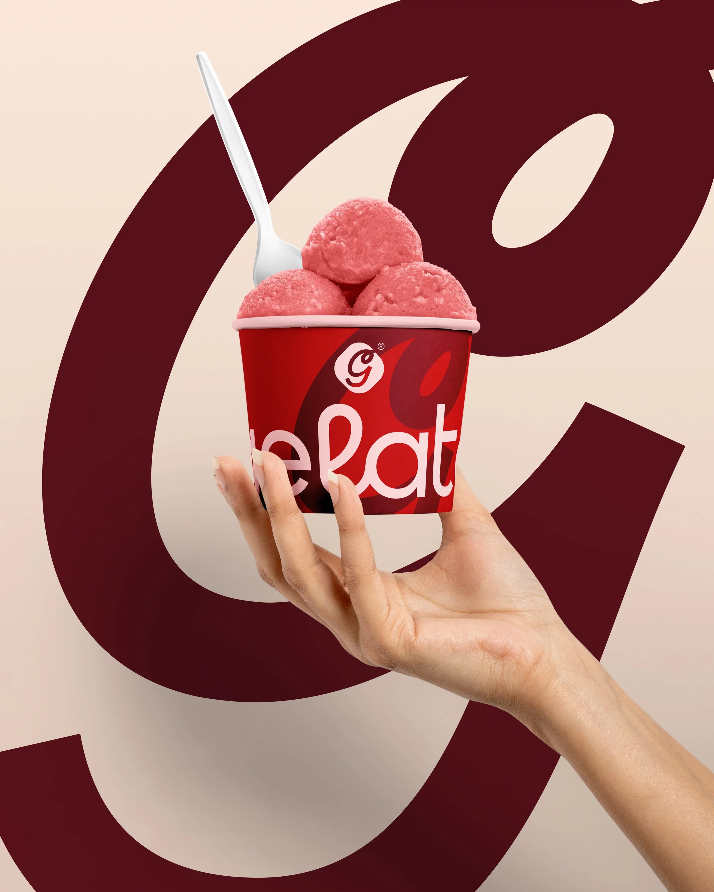 A hand holding a red cup with the word 'dunkin' printed on it. The cup contains three pink scoops of ice cream or frozen dessert. A white spoon is inserted into one of the scoops. The background features a large, abstract, dark red 'D' logo on a ligh