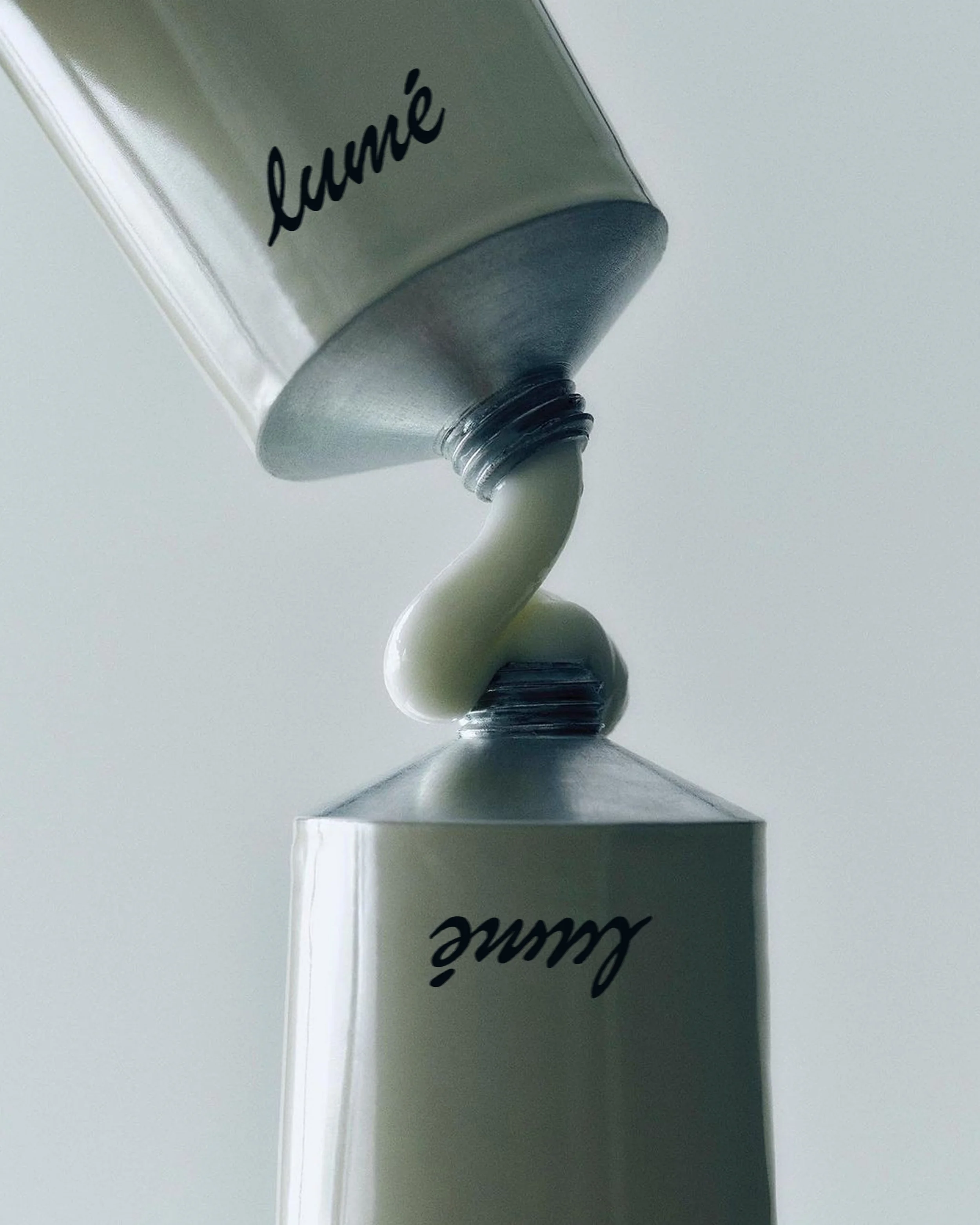 Close-up of a metallic tube with the word 'lauré' in cursive, pouring white cream into a container, on a plain white surface.