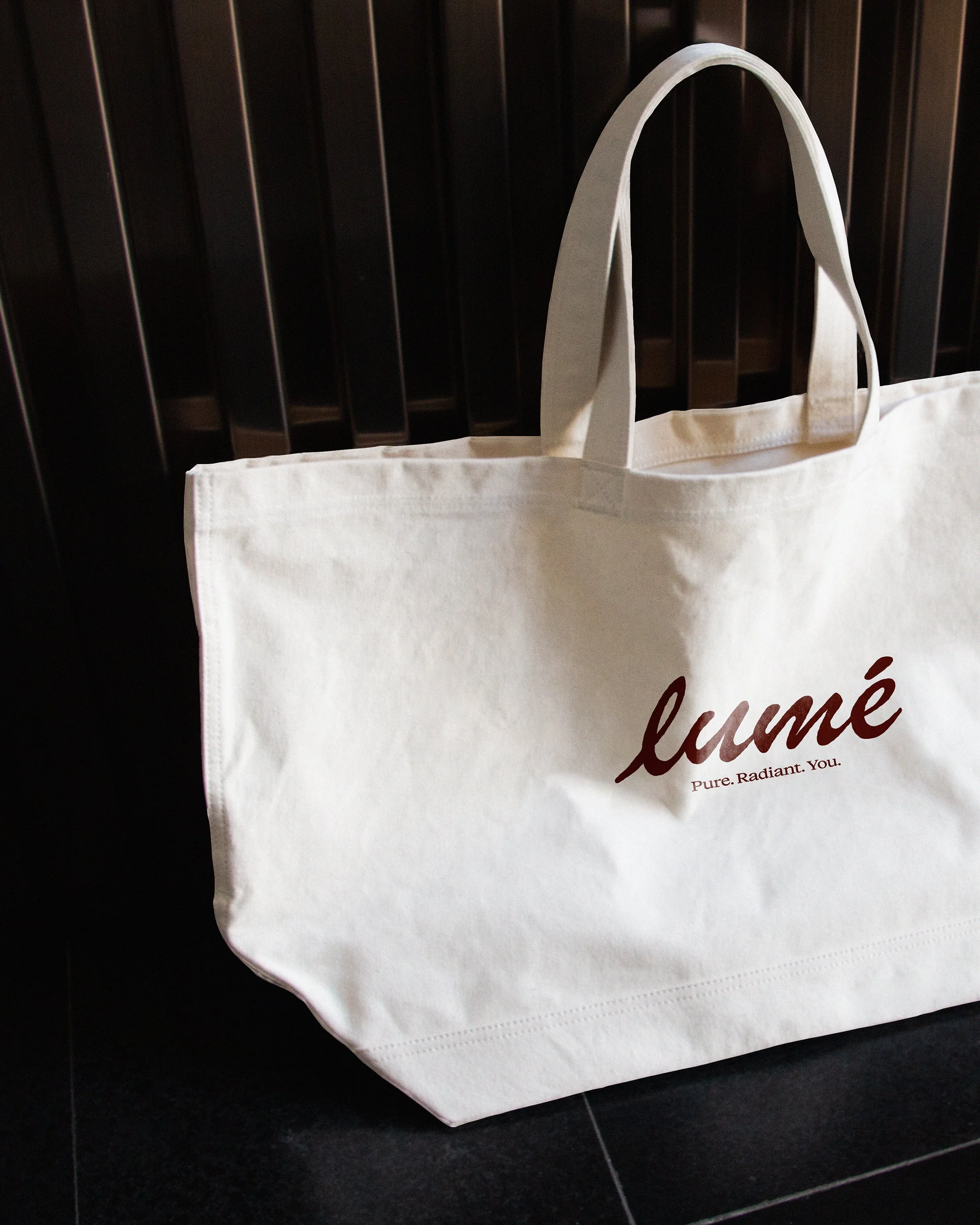 A white tote bag with the word "lume" printed on it, placed against a dark background.