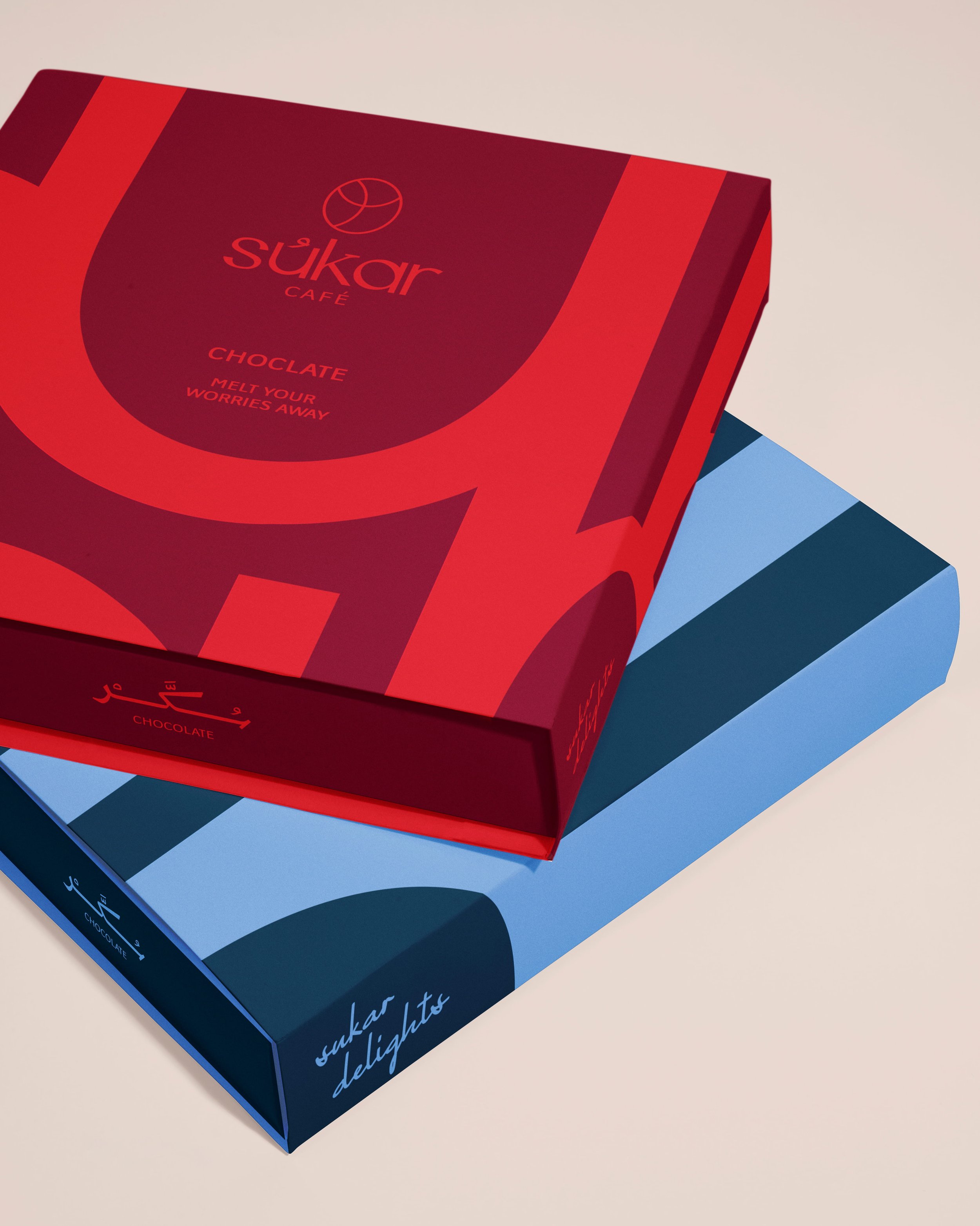 Two boxes of Sukar Café chocolates, one red with the word 'chocolate' and 'melt your worries away,' and the other blue with the same text, placed on a white surface.