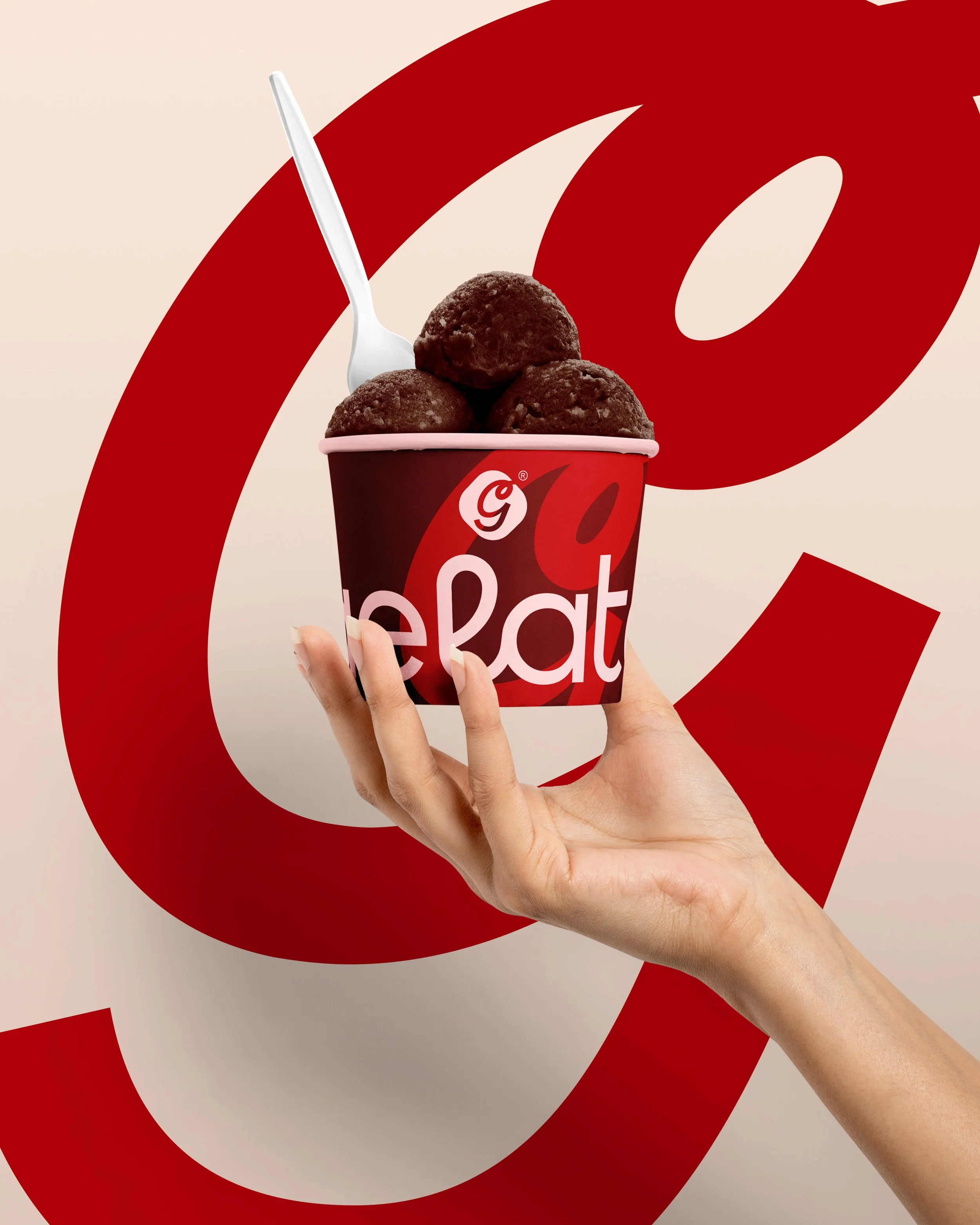 A hand holding a cup of chocolate ice cream balls with a white spoon against a beige background with large red swoosh design.