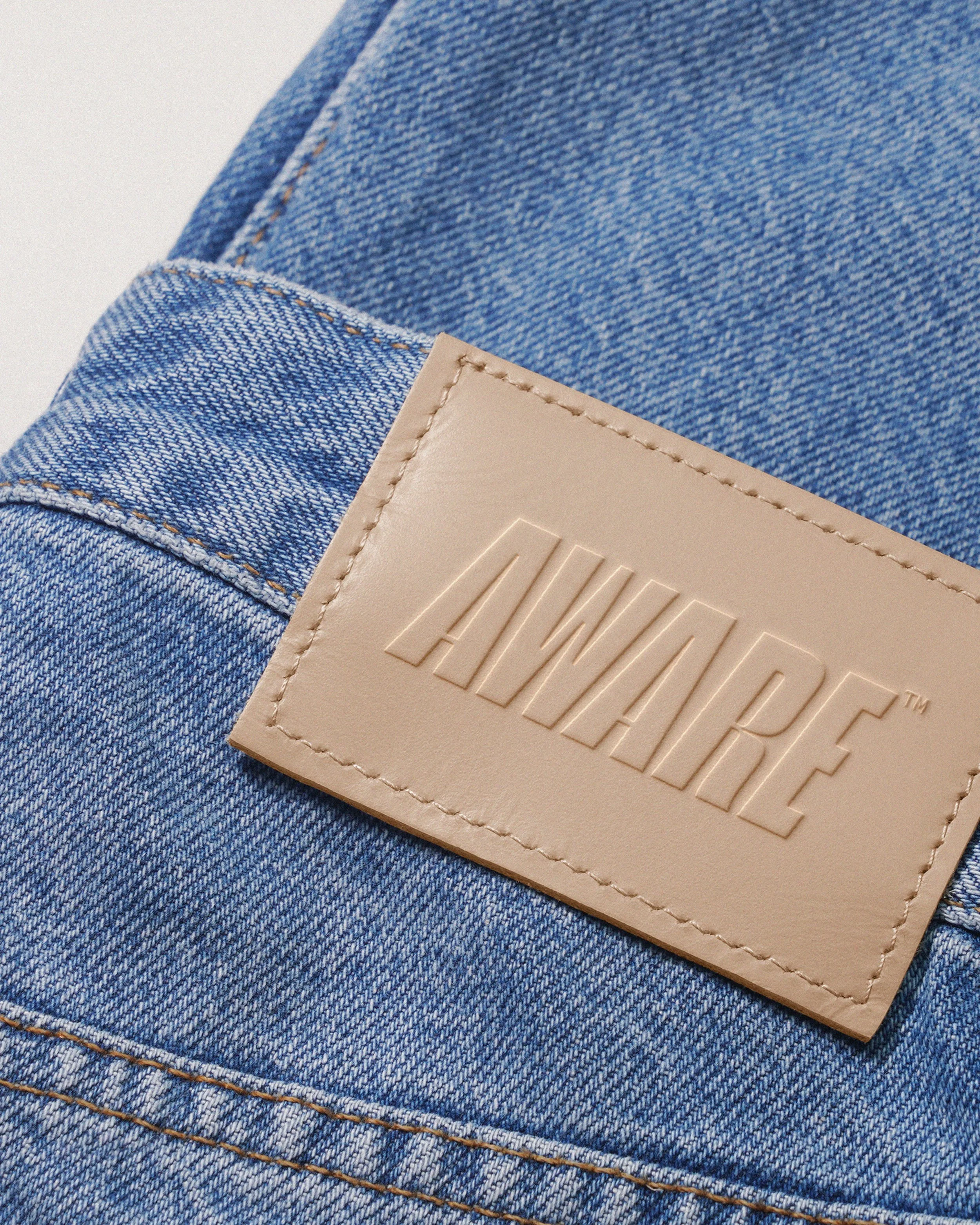 Close-up of a pair of blue denim jeans with visible stitching and a beige leather label with embossed text.