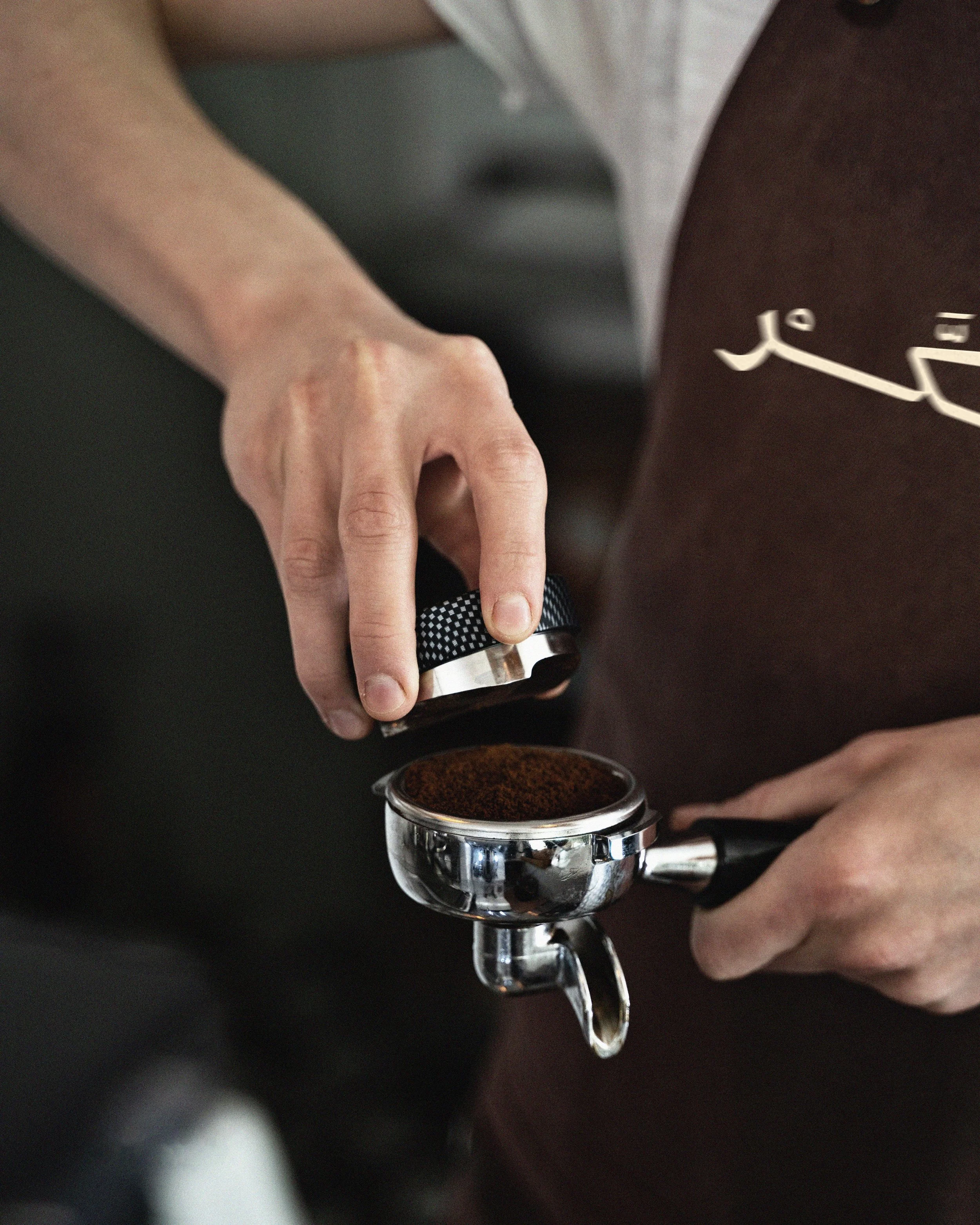 Close-up of a person’s hand pressing a button on a portafilter, with coffee being brewed into a cup underneath.