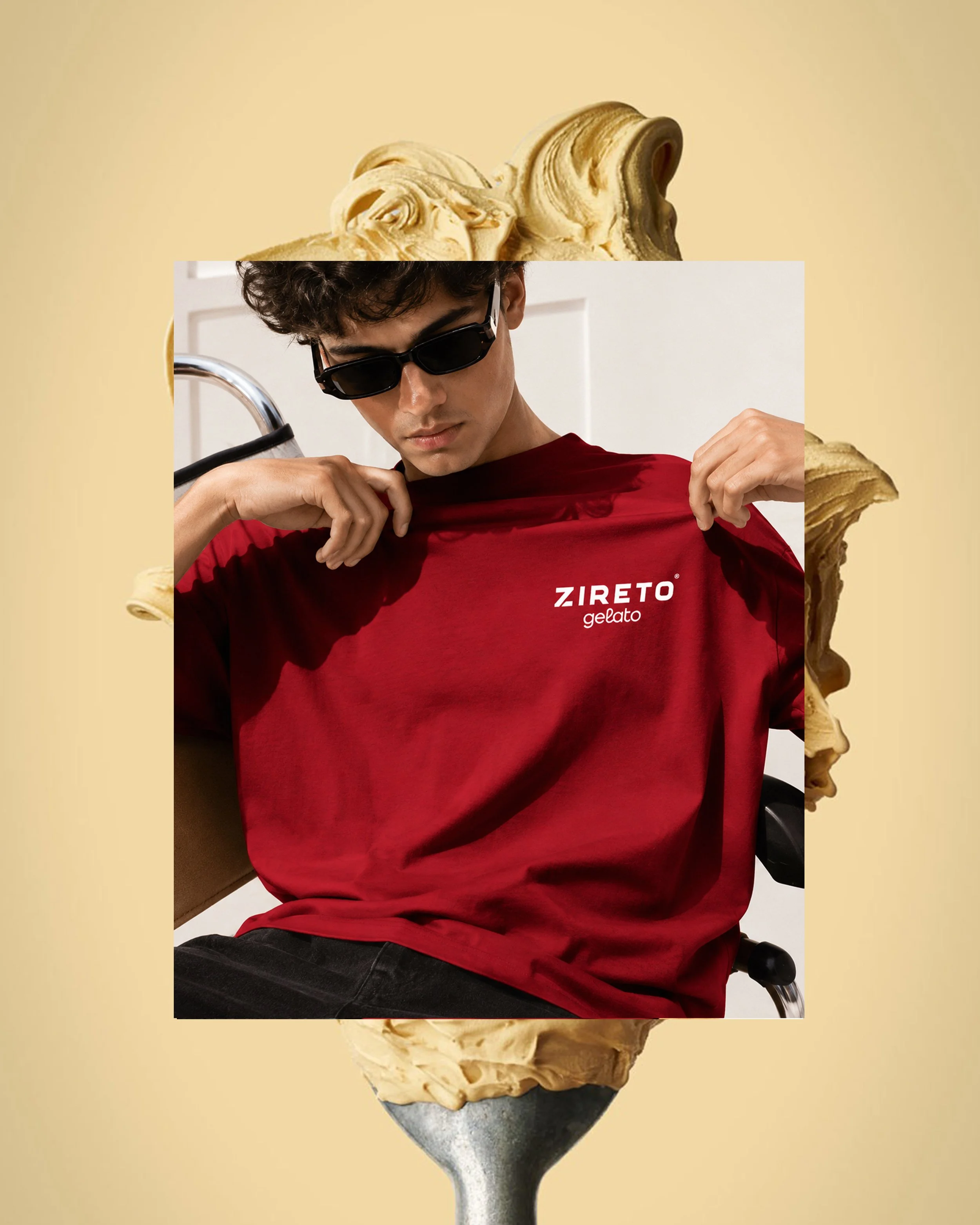 A person with curly hair wearing sunglasses and a red shirt, sitting in a wheelchair, has ice cream on their head and around their neck.
