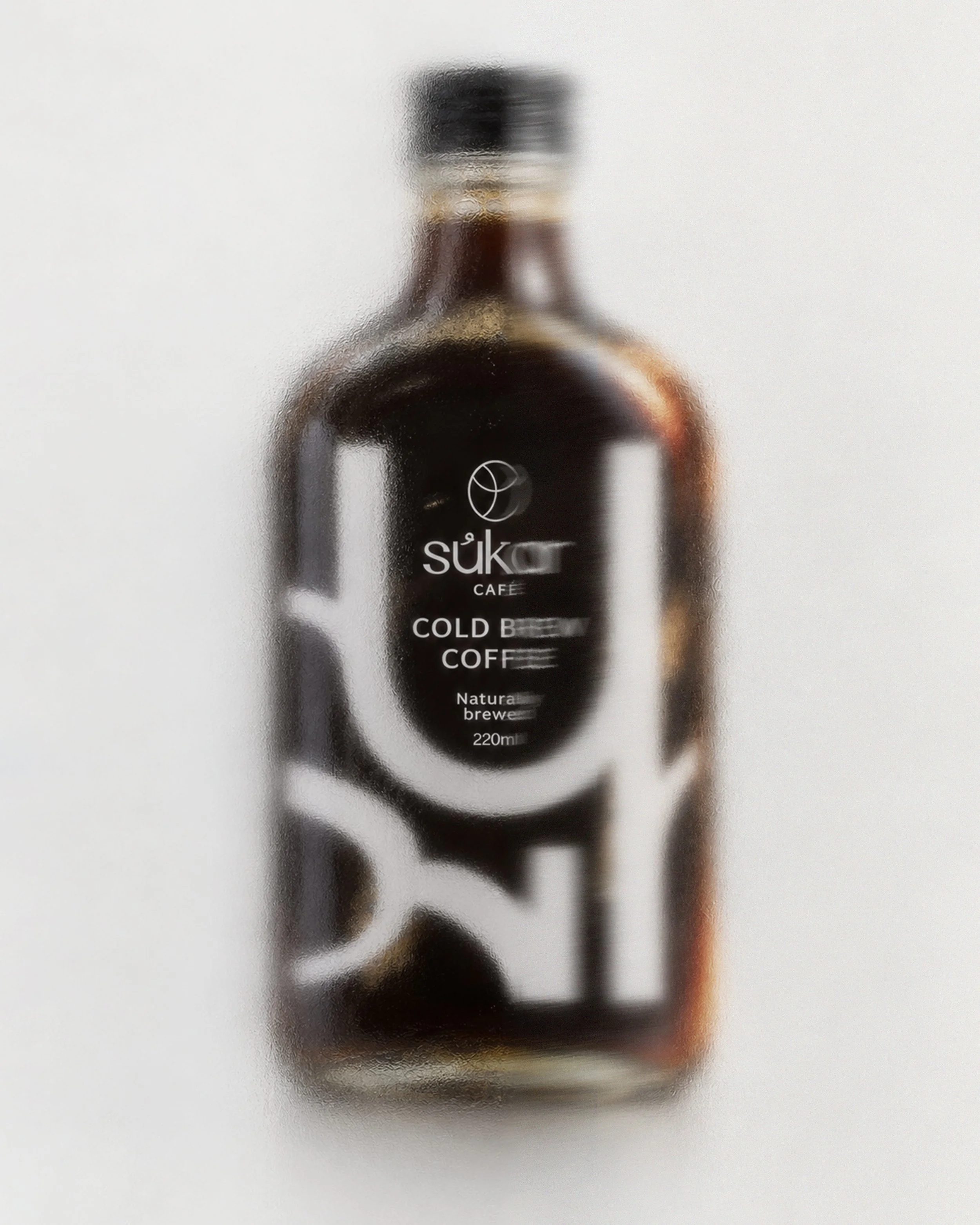 Blurred image of a bottle with a label that reads 'suk Café Cold Brew Coffee' and a white background.