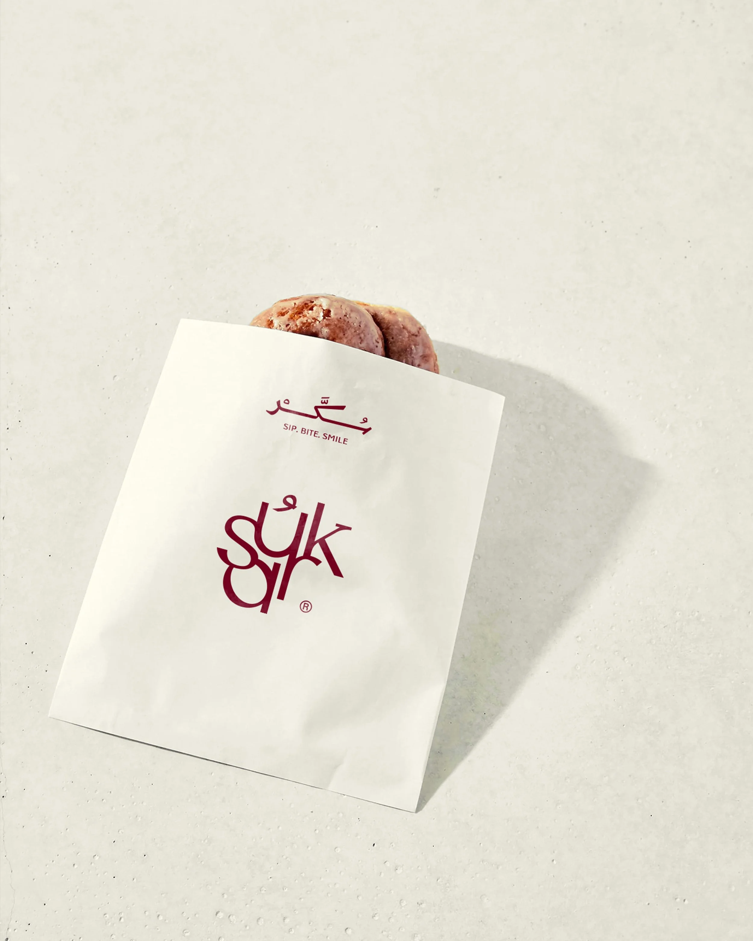 A partially visible white paper with red Arabic writing and the words 'SIP. BITE. SMILE' on a white textured surface.