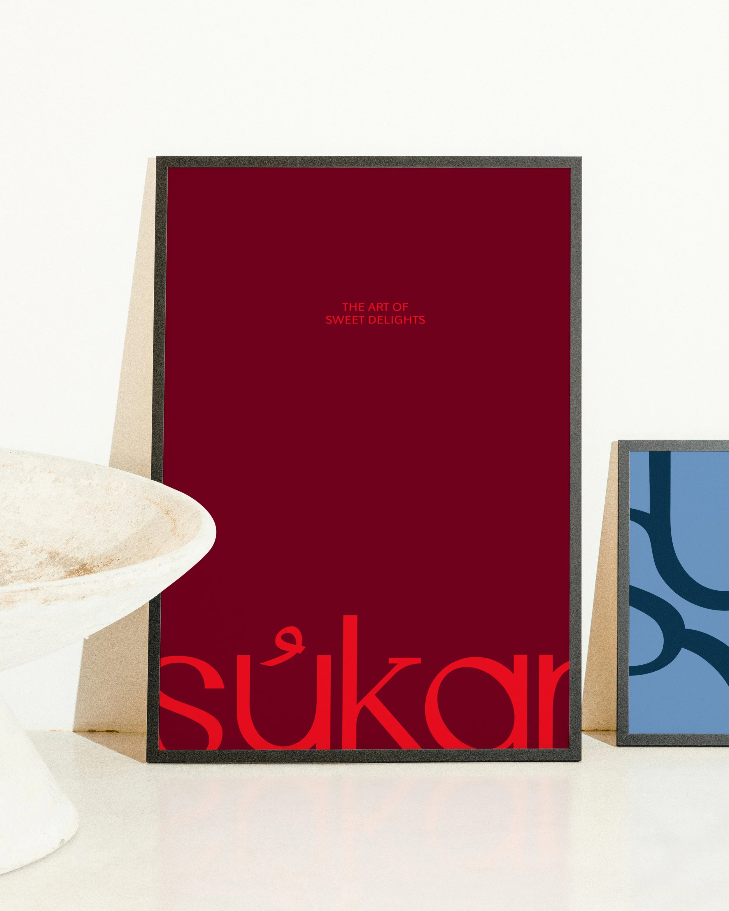Three framed posters on a white wall, with the middle one showing red text that reads 'THE ART OF SÜßKUCHEN' on a dark red background, and the right poster partly visible with blue and white design elements.