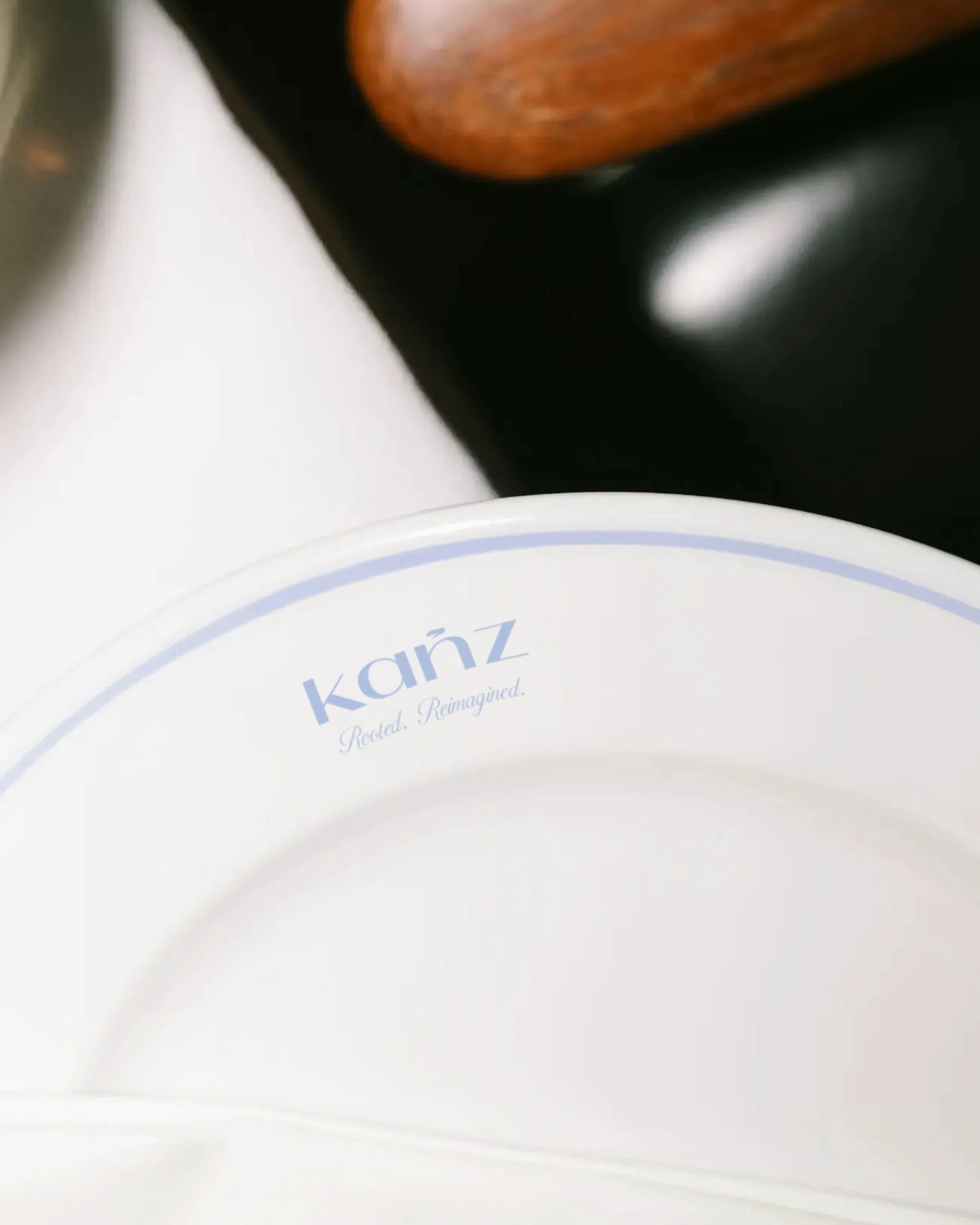 Close-up of a white surface with part of a blue and white object, possibly a plate or coaster, and a black object, with a wooden item in the background. The scene is blurry.