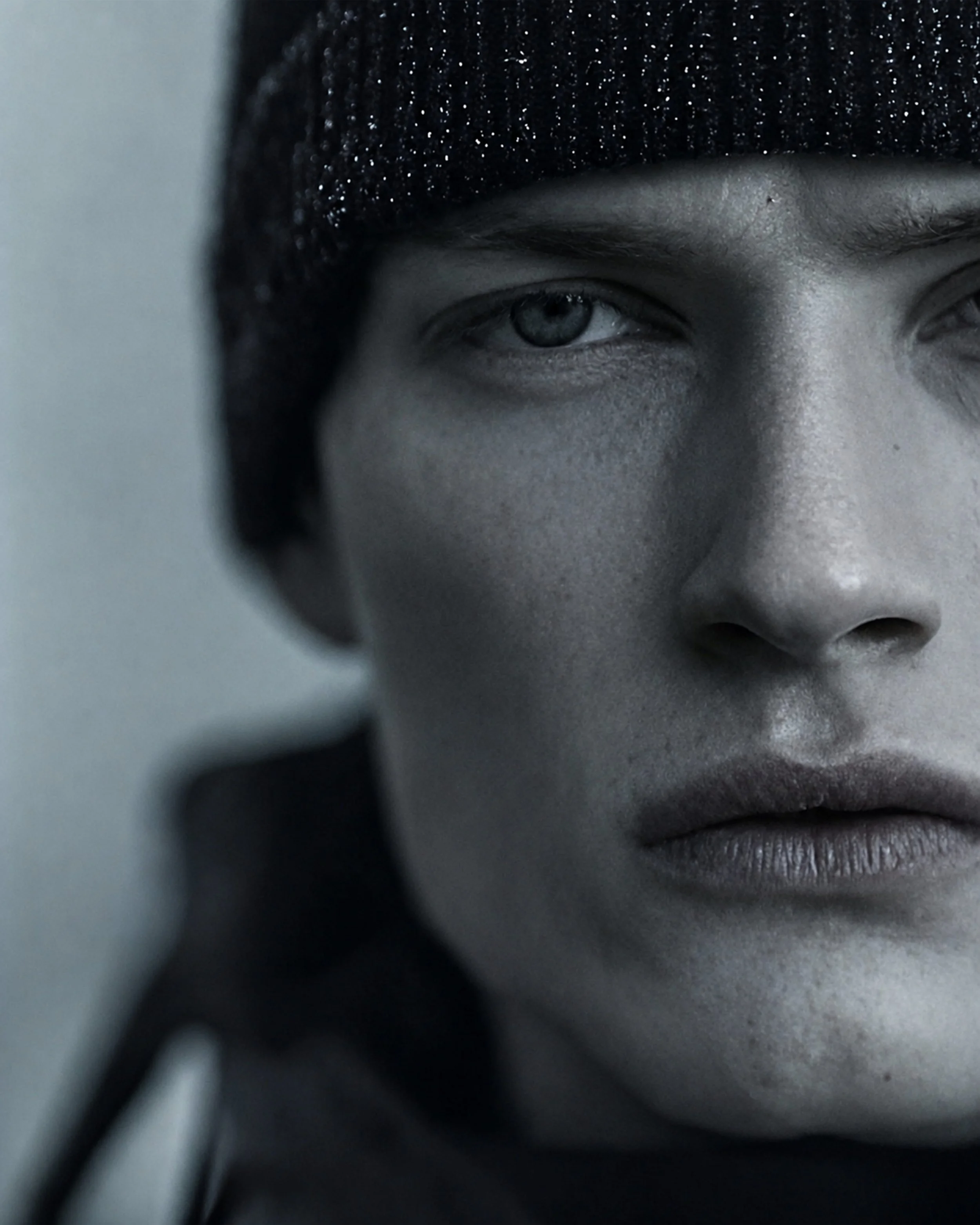 Close-up of a person's face, focusing on one eye, wearing a black knit beanie, with a neutral expression.