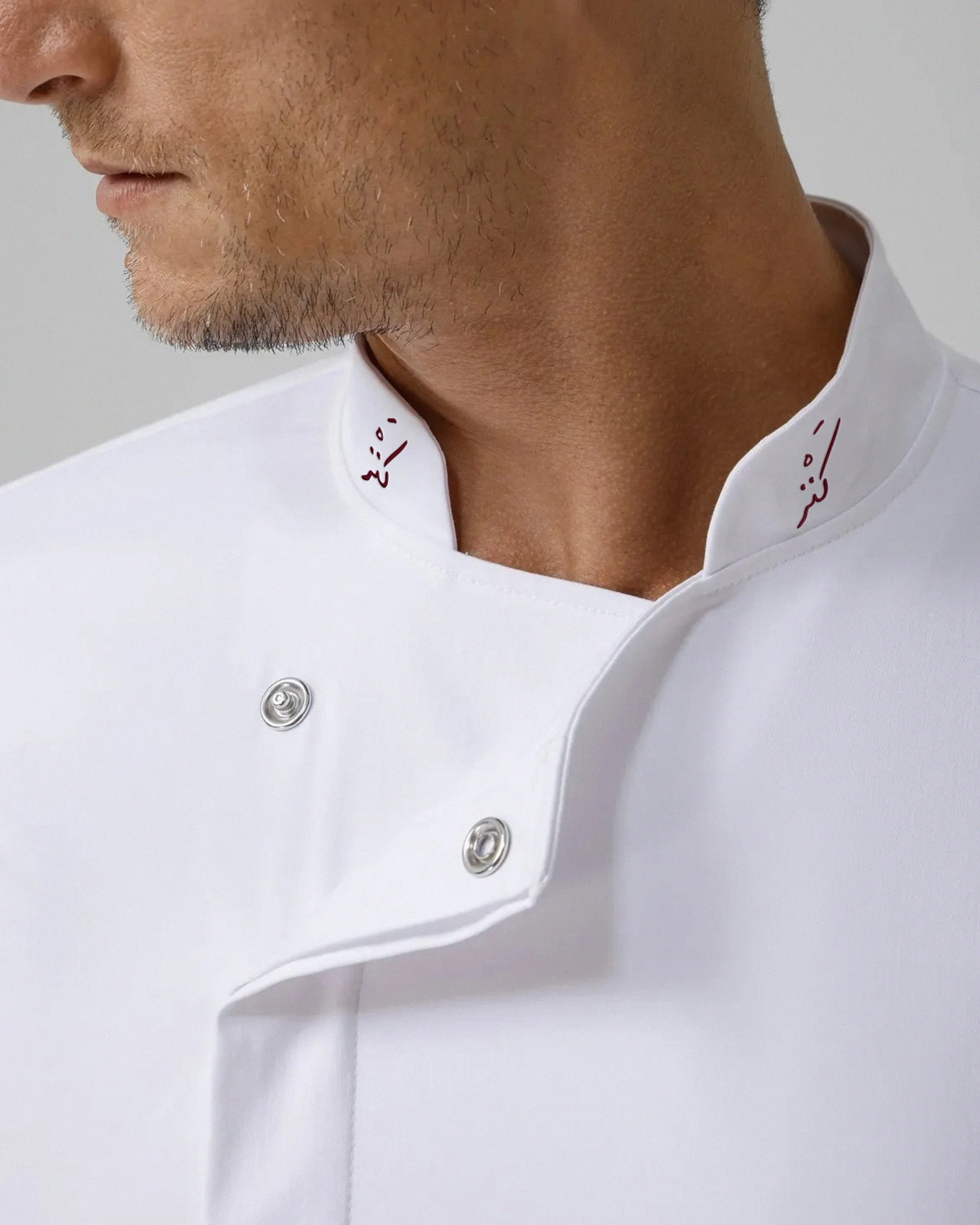 Close-up of a man's neck and lower face, wearing a white collared shirt with red writing on the collar, against a plain background.
