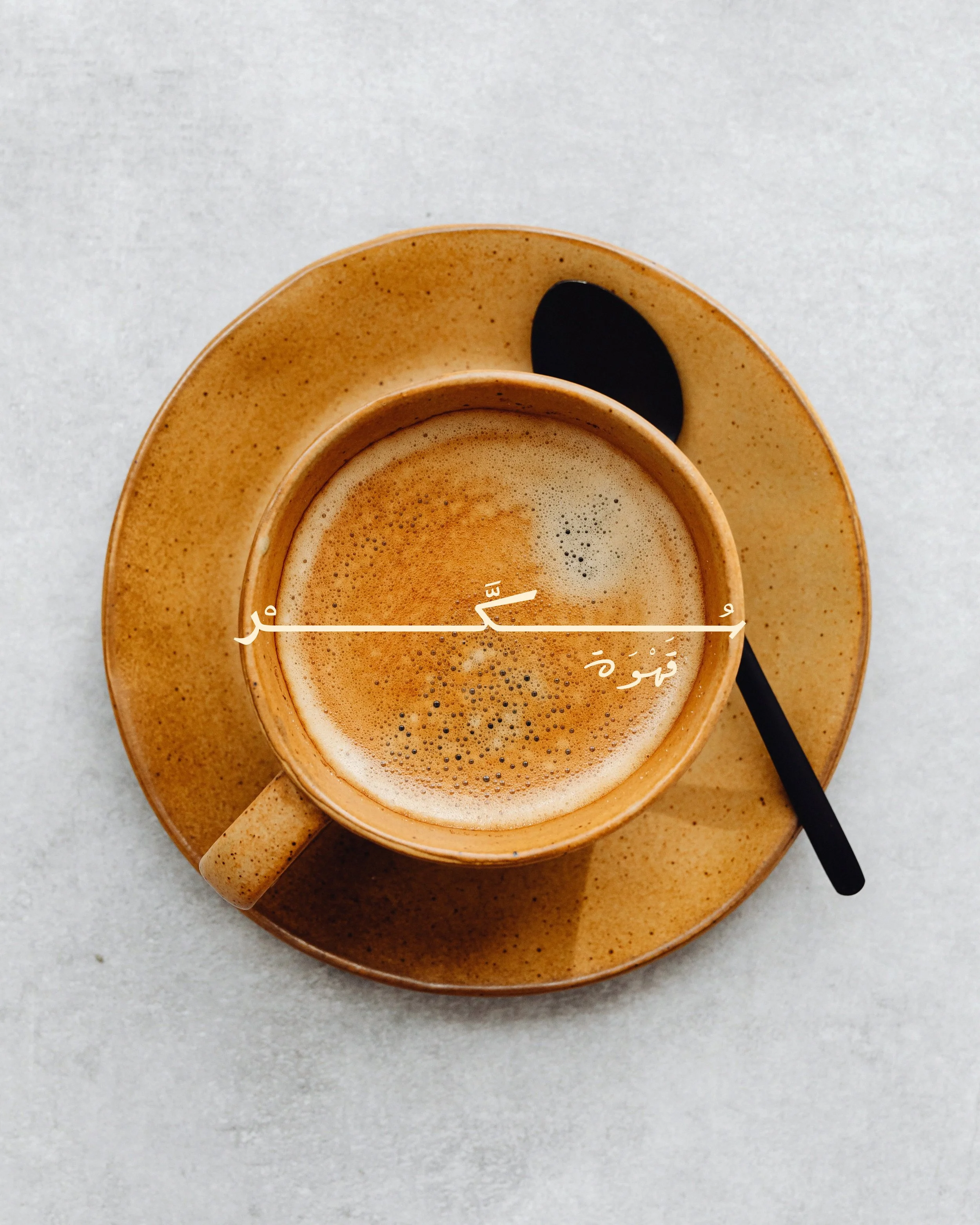 Close-up of a cup of coffee with foam and bubbles, placed on a matching saucer on a light gray surface.
